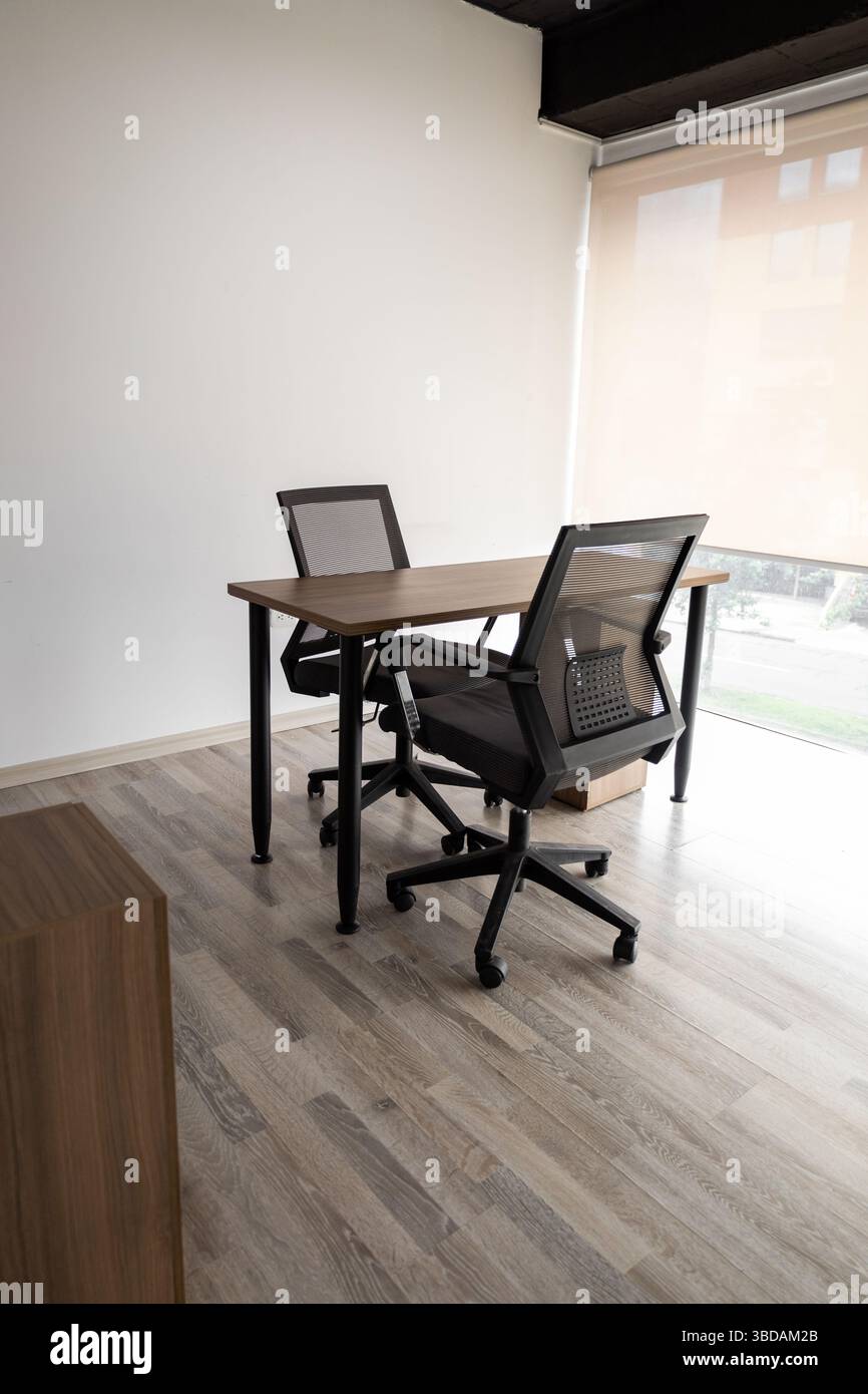 Ein moderner, privater Tagungsraum mit zwei schwarzen Stühlen um einen kleinen Tisch, umgeben von Glaswänden, ideal für konzentrierte Gespräche und Zusammenarbeit. Stockfoto