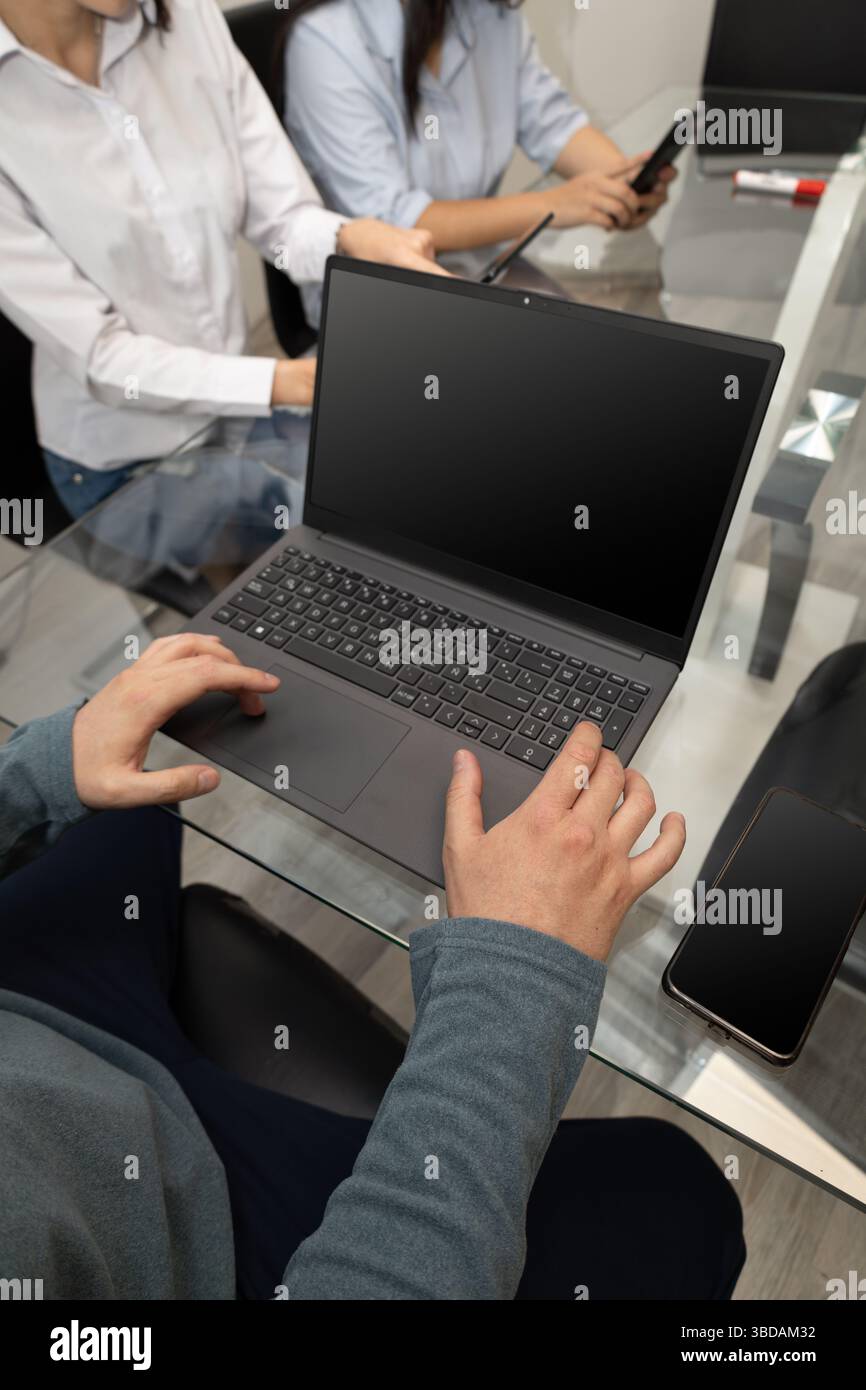 Ein Manager prüft wichtige Berichte auf dem Computer, während zwei Mitarbeiter neben ihm am Tisch warten, was Teamarbeit, Führungsstärke und kritisches t symbolisiert Stockfoto