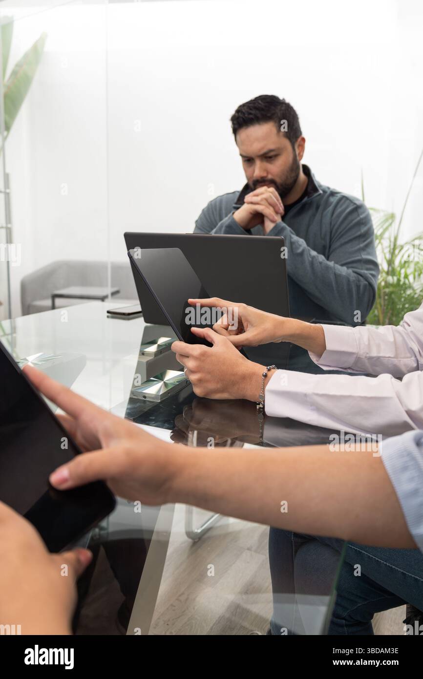 Ein Vorgesetzter sitzt sorgfältig vor einem Computer, der Daten analysiert, während zwei weibliche Mitarbeiter neben dem Tisch warten, um Teamarbeit und Entscheidungsgedanken widerzuspiegeln Stockfoto
