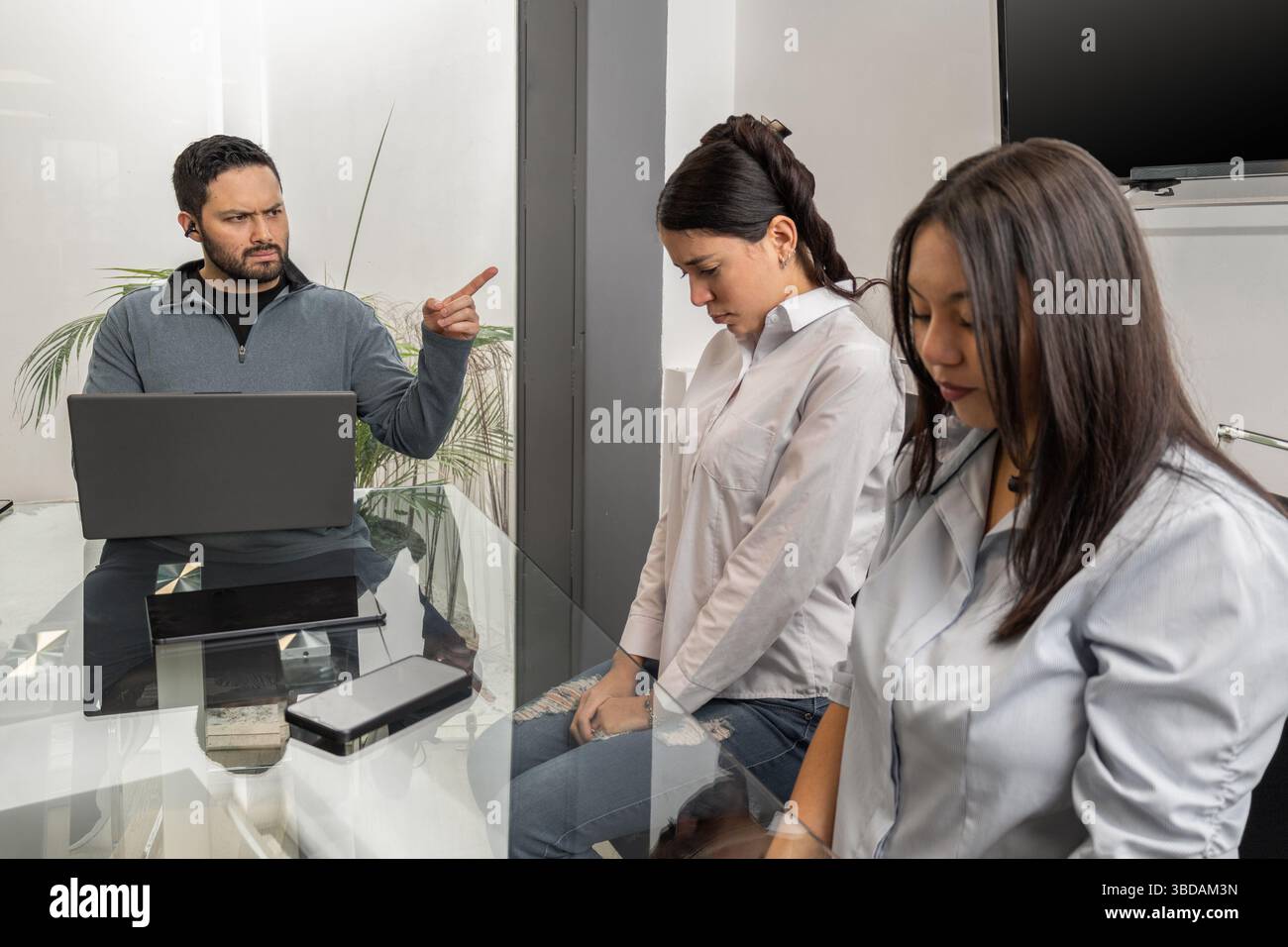 Ein seriöser Vorgesetzter konfrontiert zwei weibliche Mitarbeiter in einem modernen Büro und hebt die Spannungen am Arbeitsplatz, Kommunikationsprobleme und berufliche Herausforderungen hervor. Stockfoto