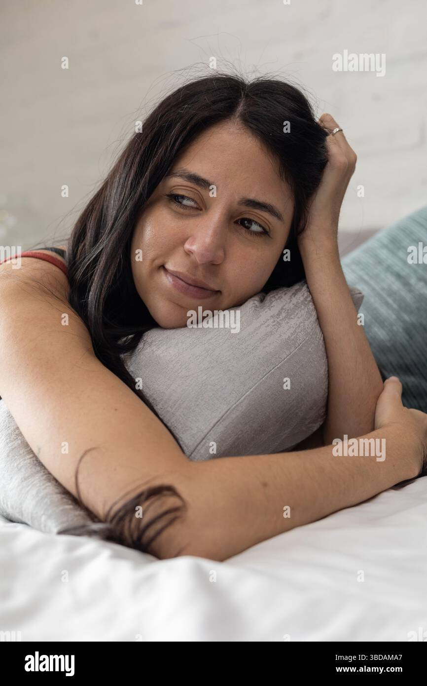 Mit dem Gesicht nach unten liegend, mit einer Hand ihren Kopf, umarmt sie das Kissen, verloren in Erinnerung oder tiefem Denken, still und still. Stockfoto