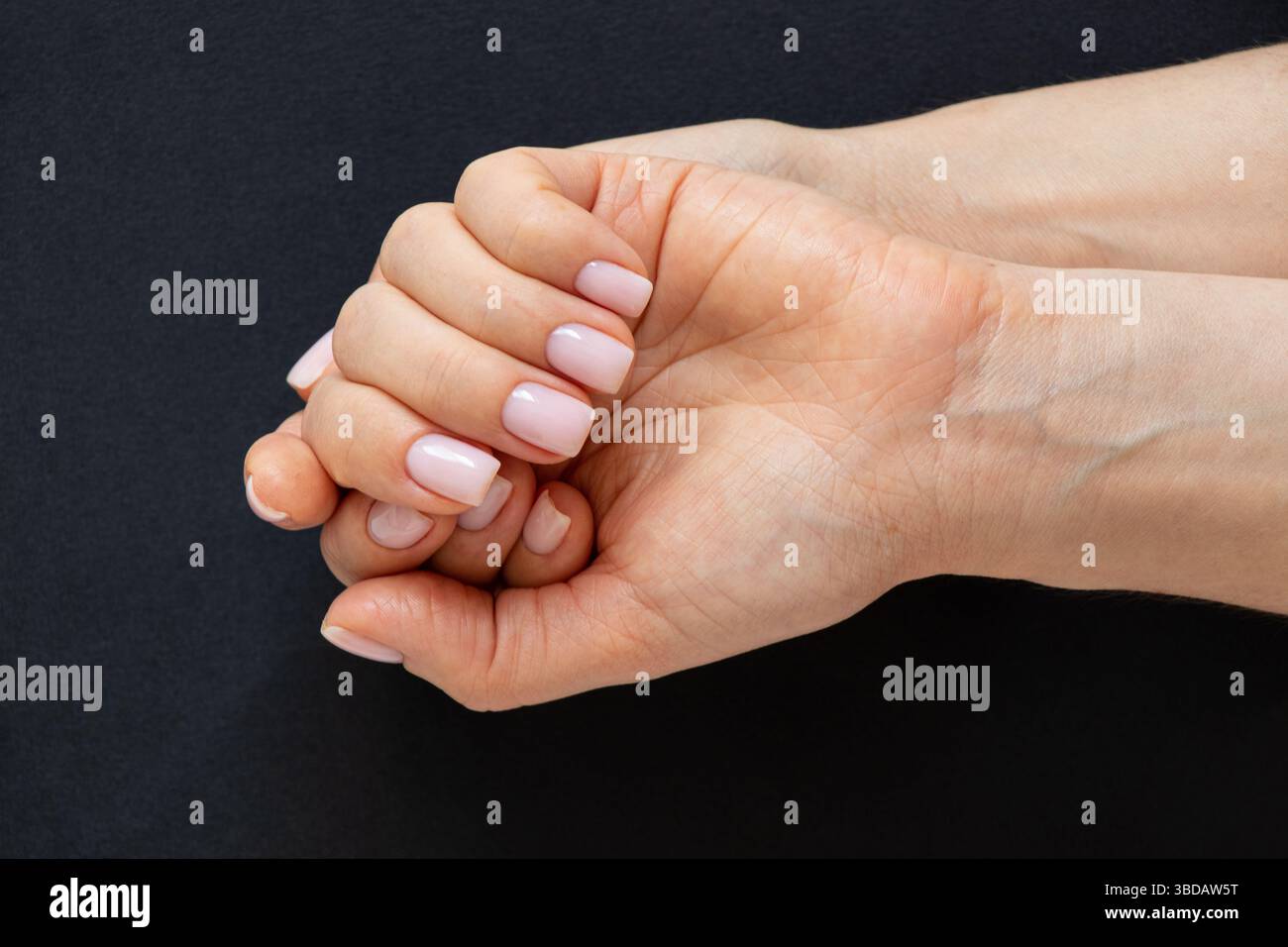 Damenhände mit einer zarten leichten Maniküre auf schwarzem Hintergrund, Hand- und Nagelpflege Stockfoto