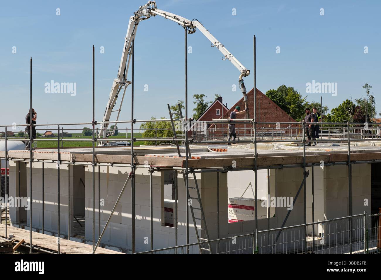 30. April 2025 - Stavenisse-Niederlande: Arbeiter gießen auf einer Baustelle in einem niederländischen Dorf, umgeben von Grün, Beton in einen Boden mit einem Pumpwagen Stockfoto