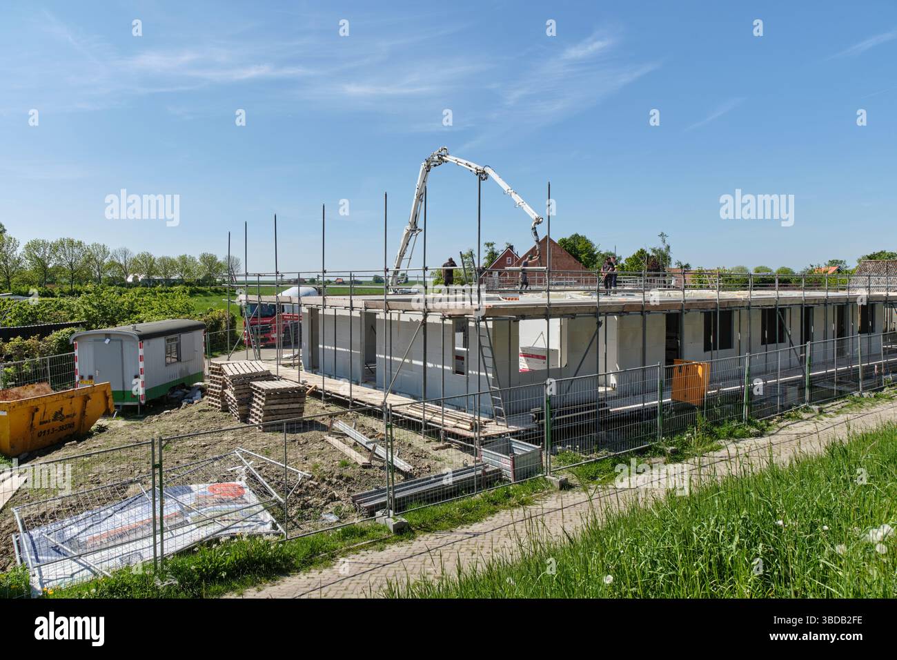 30. April 2025 - Stavenisse-Niederlande: Arbeiter gießen auf einer Baustelle in einem niederländischen Dorf, umgeben von Grün, Beton in einen Boden mit einem Pumpwagen Stockfoto