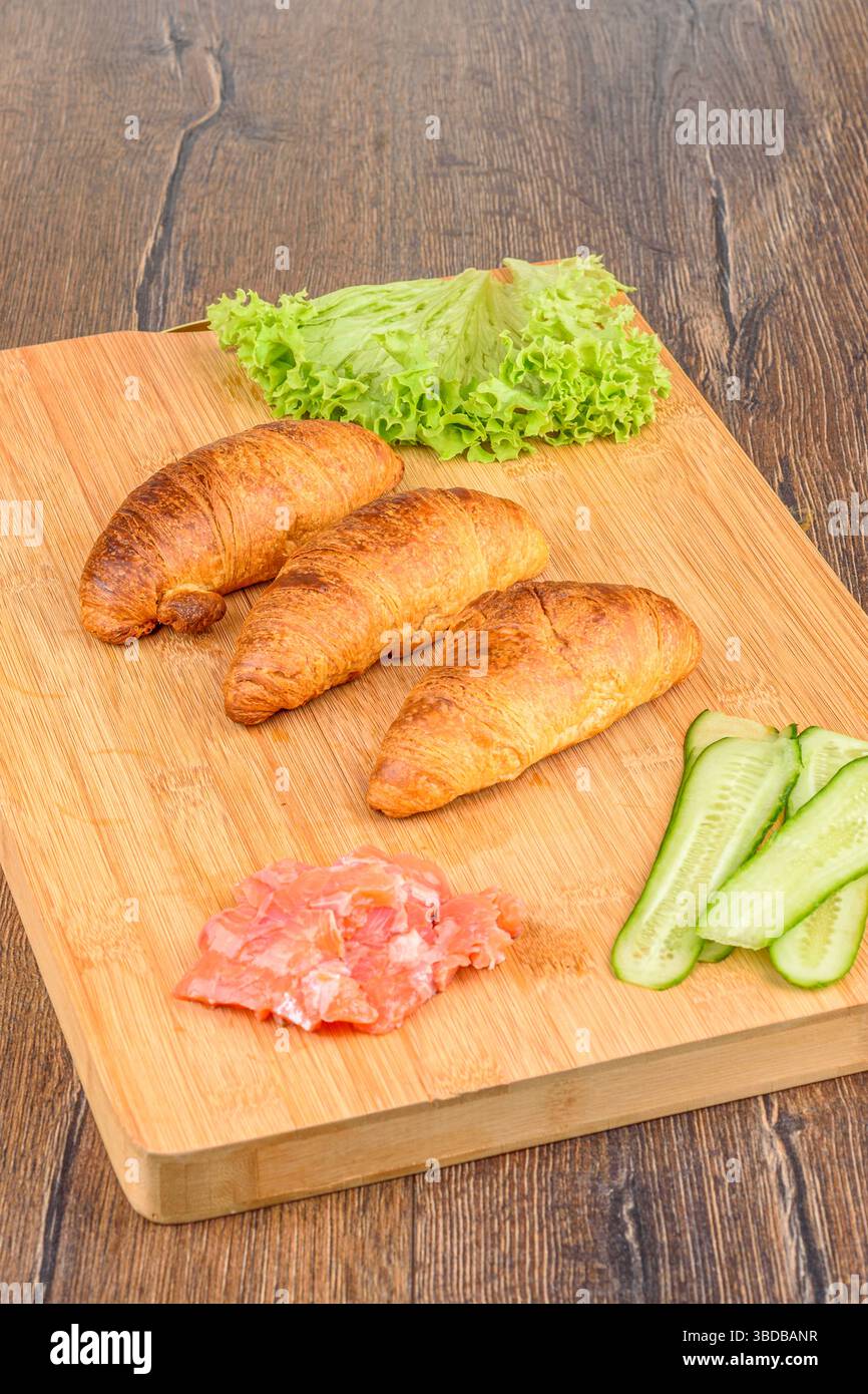 Croissants und Zutaten für die Füllung mit Salatblättern, rotem Fisch und Gurken. Hausmannskost. Stockfoto