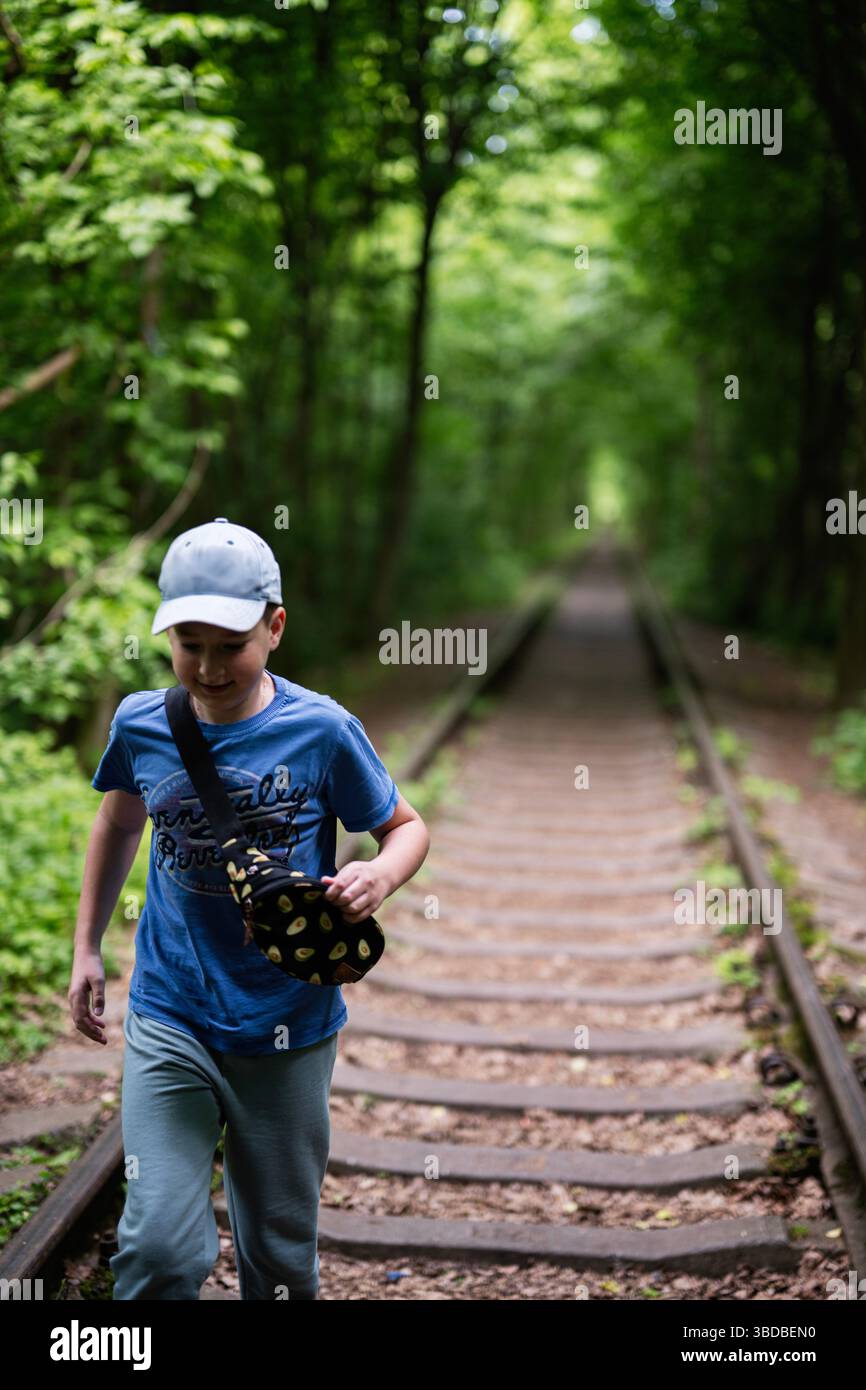 Kinder überqueren verlassene Bahngleise in einem ruhigen, grünen Waldgebiet im Freien. Stockfoto