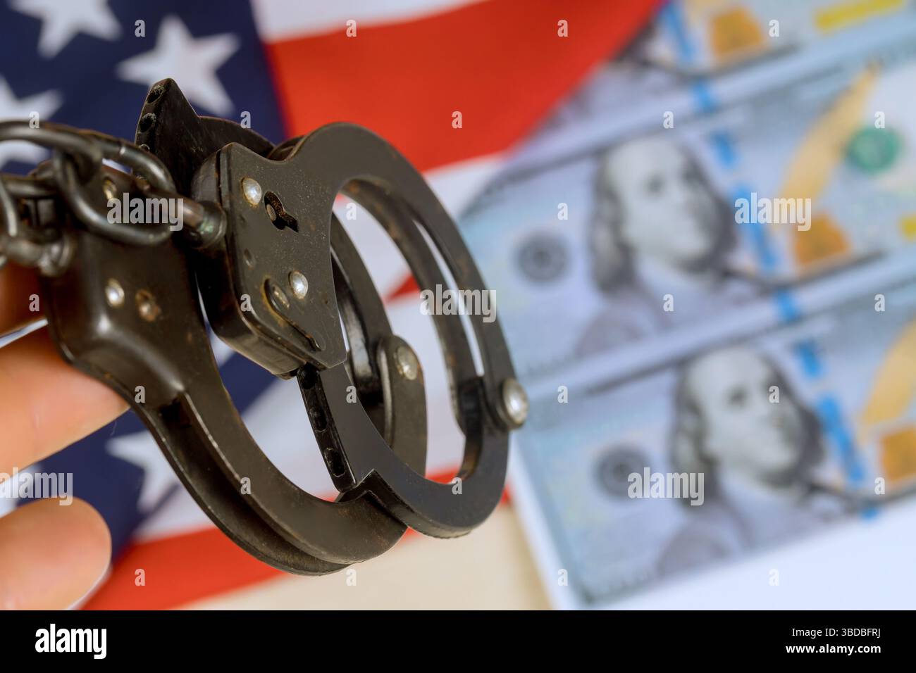 Handschellen, die fest mit gefälschtem US-Geld im Hintergrund gehalten werden. Ernste Stimmung spiegelt die vorsichtige Besorgnis wider Stockfoto