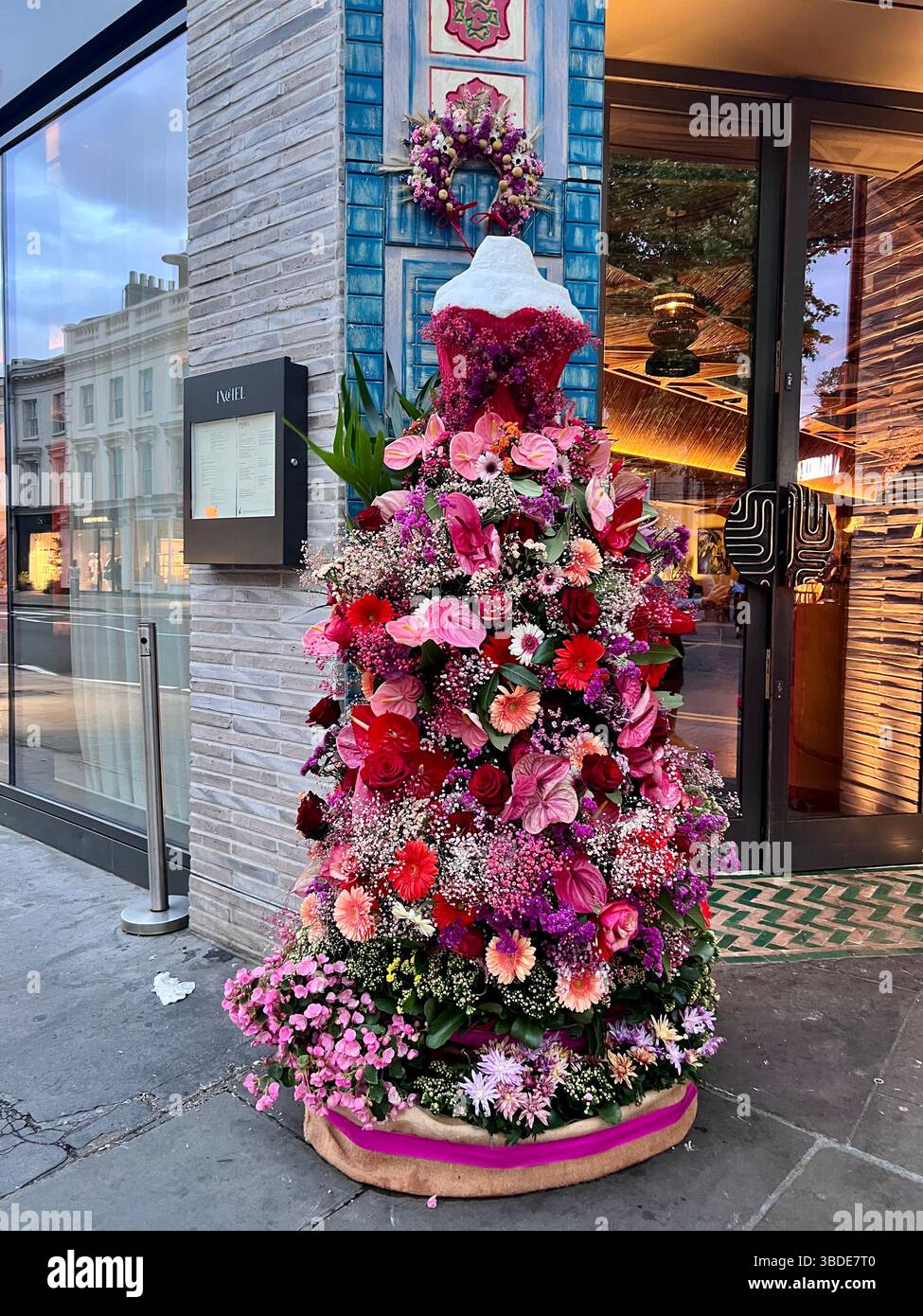 London, Chelsea in Bloom 2025 Blumenausstellung. Weibliche Schaufensterpuppe, bedeckt mit roten und rosa Blumen, um ein Kleid zu bilden. Rosen, Gerber Daisies, Flamingo Lily. Stockfoto