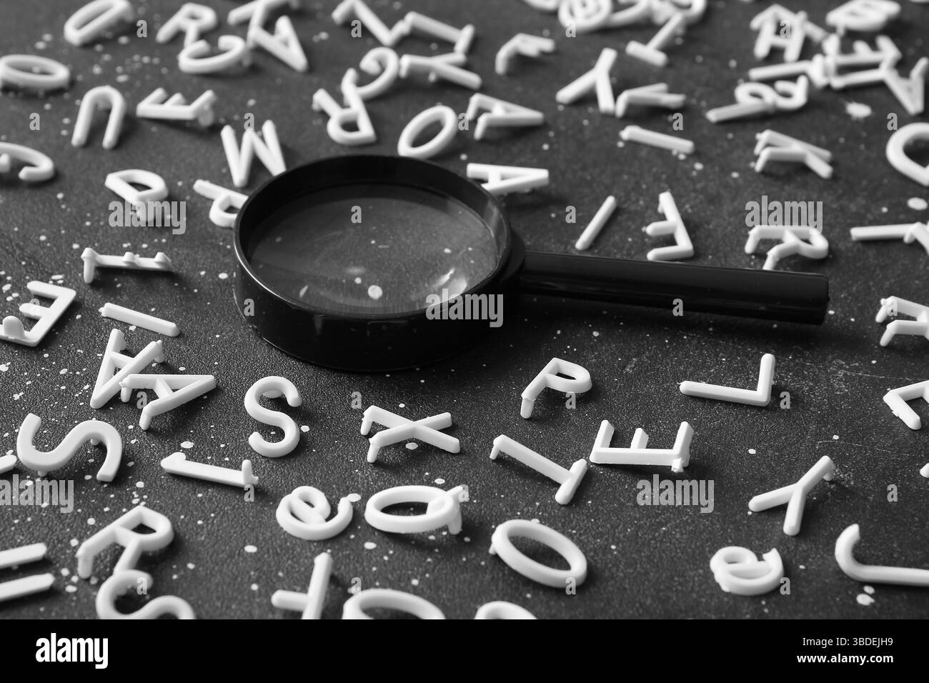 Viele englische Buchstaben und Lupe auf dunklem Hintergrund Stockfoto