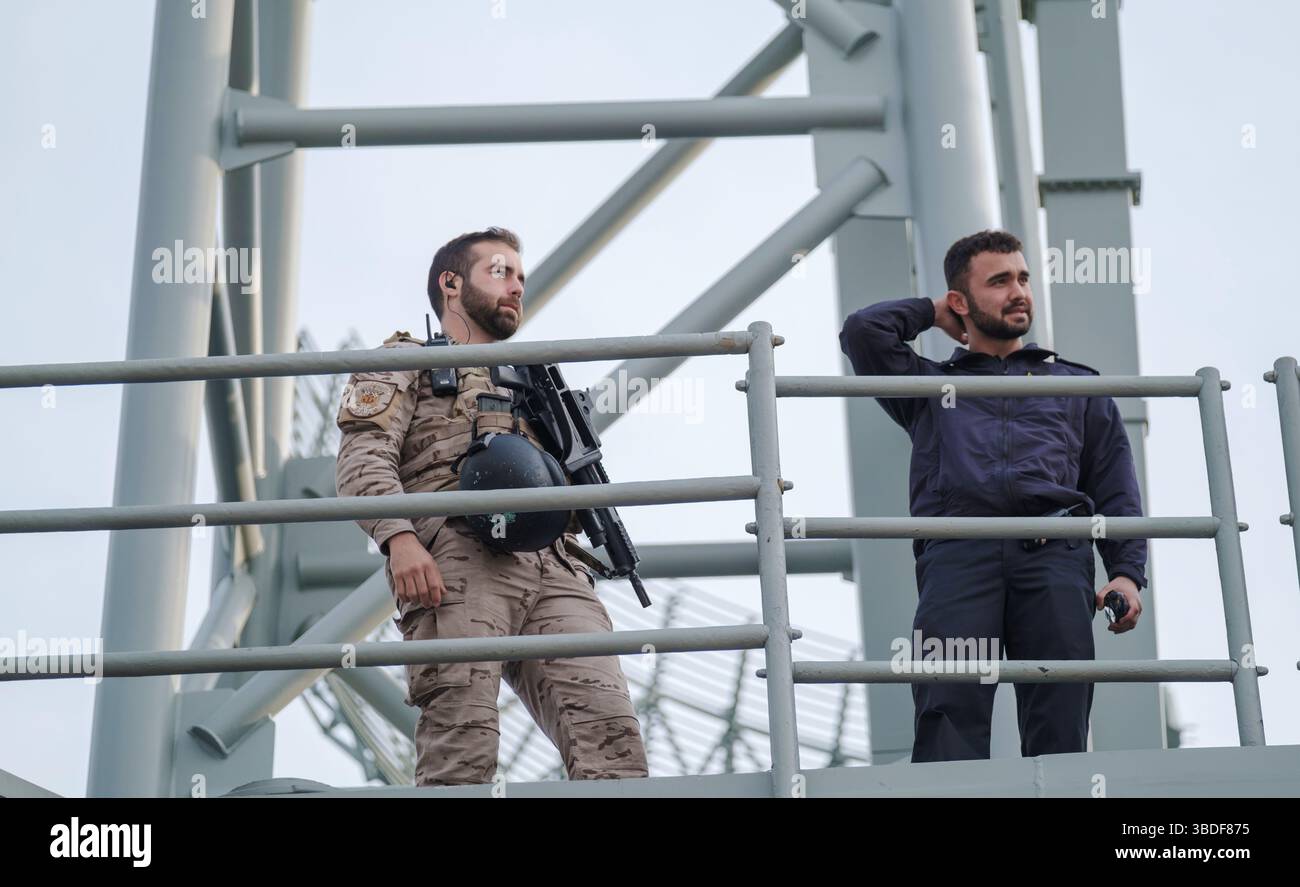 Spanien Malaga 1 28 2024 zwei Männer auf einer Metallplattform, einer in Militäruniform mit einer Schusswaffe, was auf eine Sicherheits- oder Überwachungssituation hindeutet Stockfoto