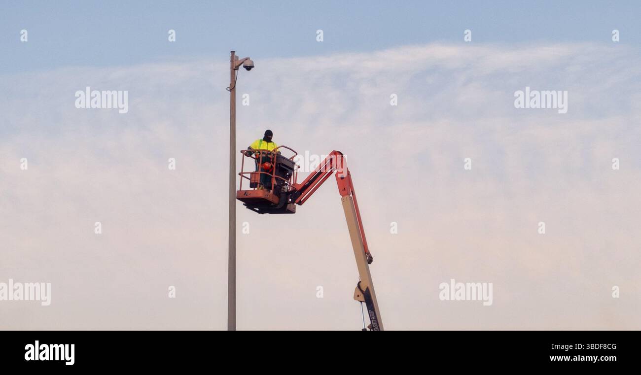 Arbeiter in Sicherheitsausrüstung, der in der Höhe auf dem Aufzug arbeitet und die Stangenausrüstung vor dem Hintergrund eines klaren Himmels wartet Stockfoto