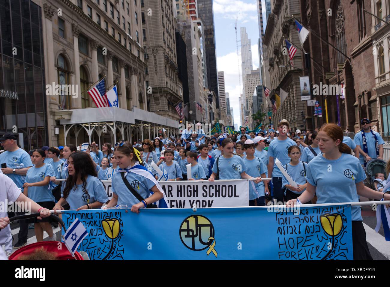 Eine große Gruppe von Teenagern und jungen Erwachsenen, die überwiegend hellblaue T-Shirts tragen, nimmt an einer Parade in einer Stadtstraße Teil. Sie tragen eine große Stockfoto
