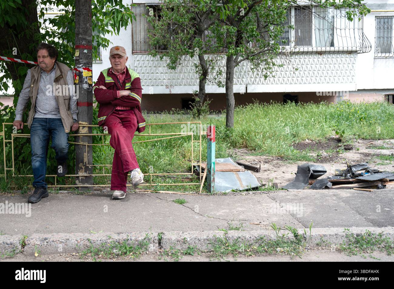 Kiew, Ukraine. Mai 2025. Zwei Männer sitzen am Zaun neben den Bruchstücken einer russischen Drohne vor einem Wohnblock im Obolonskyi-Viertel, der durch den Angriff von Trümmern während des russischen Raketen- und Drohnenangriffs am 24. Mai 2025 in Kiew, Ukraine, beschädigt wurde. Kiew und sieben andere Regionen der Ukraine wurden von einem russischen Großangriff mit 250 Schlagdrohnen und 14 ballistischen Raketen angegriffen. (Foto: Danylo Antoniuk/Ukrinform) Credit: Ukrinform/Alamy Live News Stockfoto