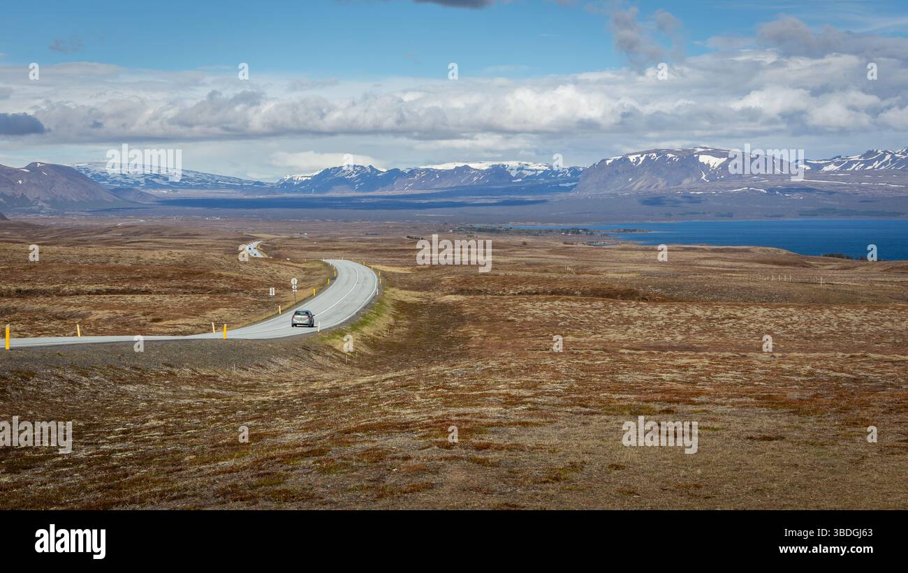Kurvenreiche Asphaltstraße 36 mit Autos, die entlang des Thingvallavatn-Sees im Thingvellir-Nationalpark, Island, Lavafeldern und schneebedeckten Bergen fahren. Stockfoto