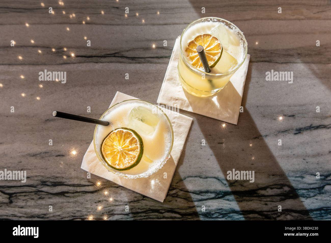 Margaritas auf einem Marmortisch mit reflektierenden Lichtern. Selektiver Fokus auf getrocknete Kalkscheibe im linken Glas Stockfoto