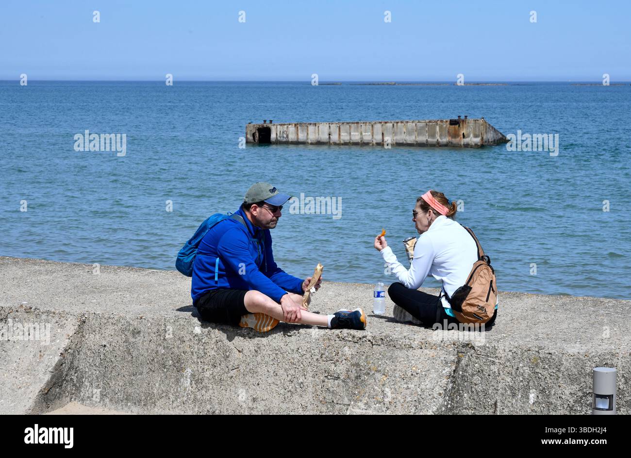 Touristen in Arromanches-les-Bains in der Normandie Frankreich mit den Überresten von Mulberry-Häfen im Meer. Stockfoto