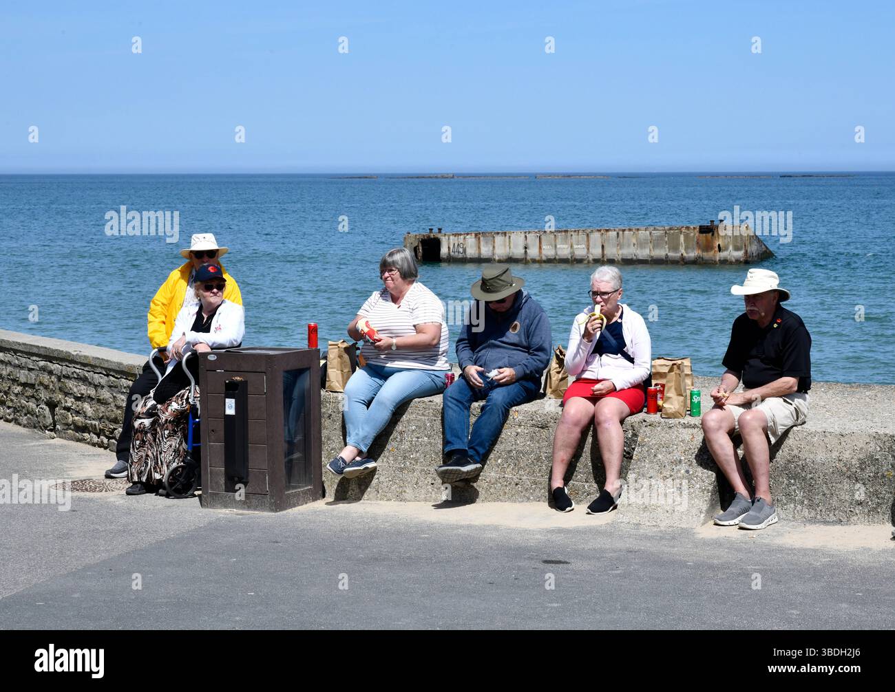 Touristen in Arromanches-les-Bains in der Normandie Frankreich mit den Überresten von Mulberry-Häfen im Meer. Stockfoto