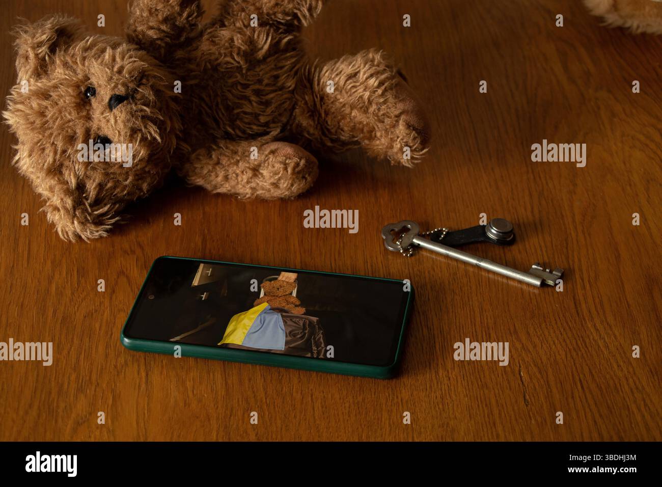 Teddybär, alter Schlüssel und Smartphone mit Foto eines Mädchens mit Koffer und ukrainischer Flagge, Abschied und Verlassen des Hauses wegen des Krieges Stockfoto