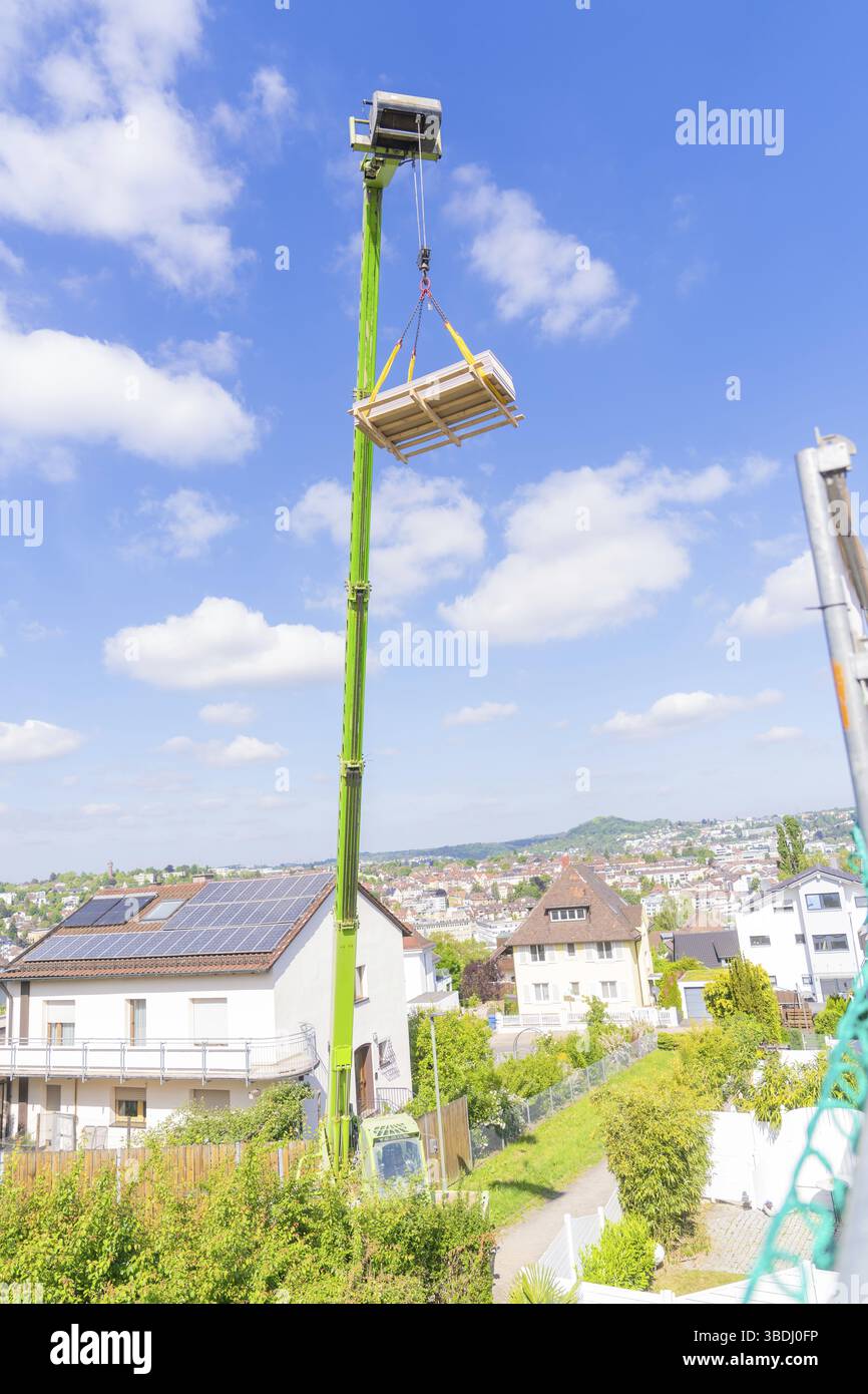 Kran hebt Holz über Häuser in Vorstadtviertel mit blauem Himmel, RABA Solar Baustelle einer Dachsanierung, Pforzheim, Deutschland, Europa Stockfoto