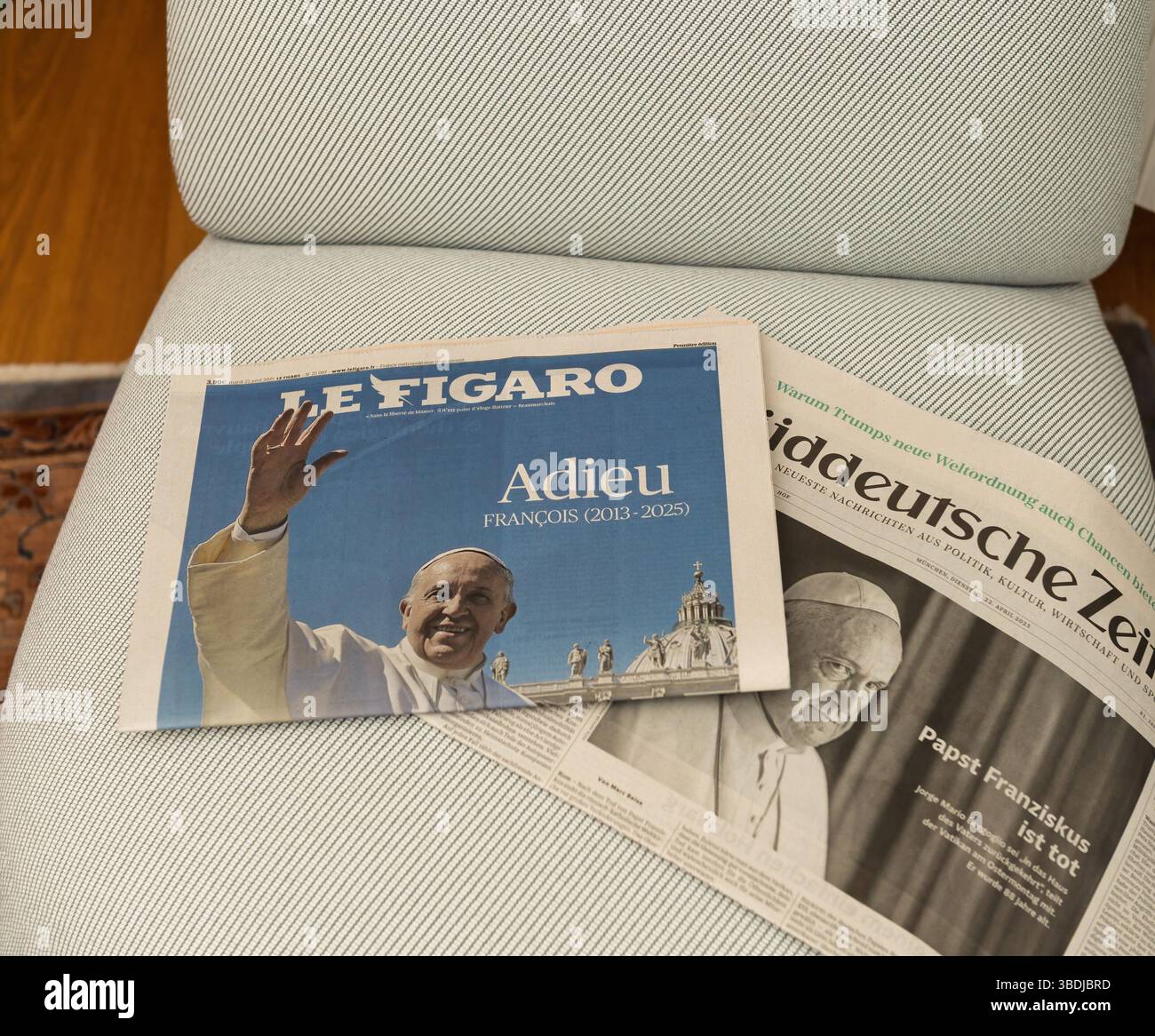 Paris, Frankreich - 22. April 2025: Zwei Zeitungen mit Papst-Franziskus-Tributen, Le Figaro und Suddeutsche Zeitung, ruhen nebeneinander auf einem strukturierten Polsterstuhl mit teilweiser Überlappung und klaren Schlagzeilen Stockfoto