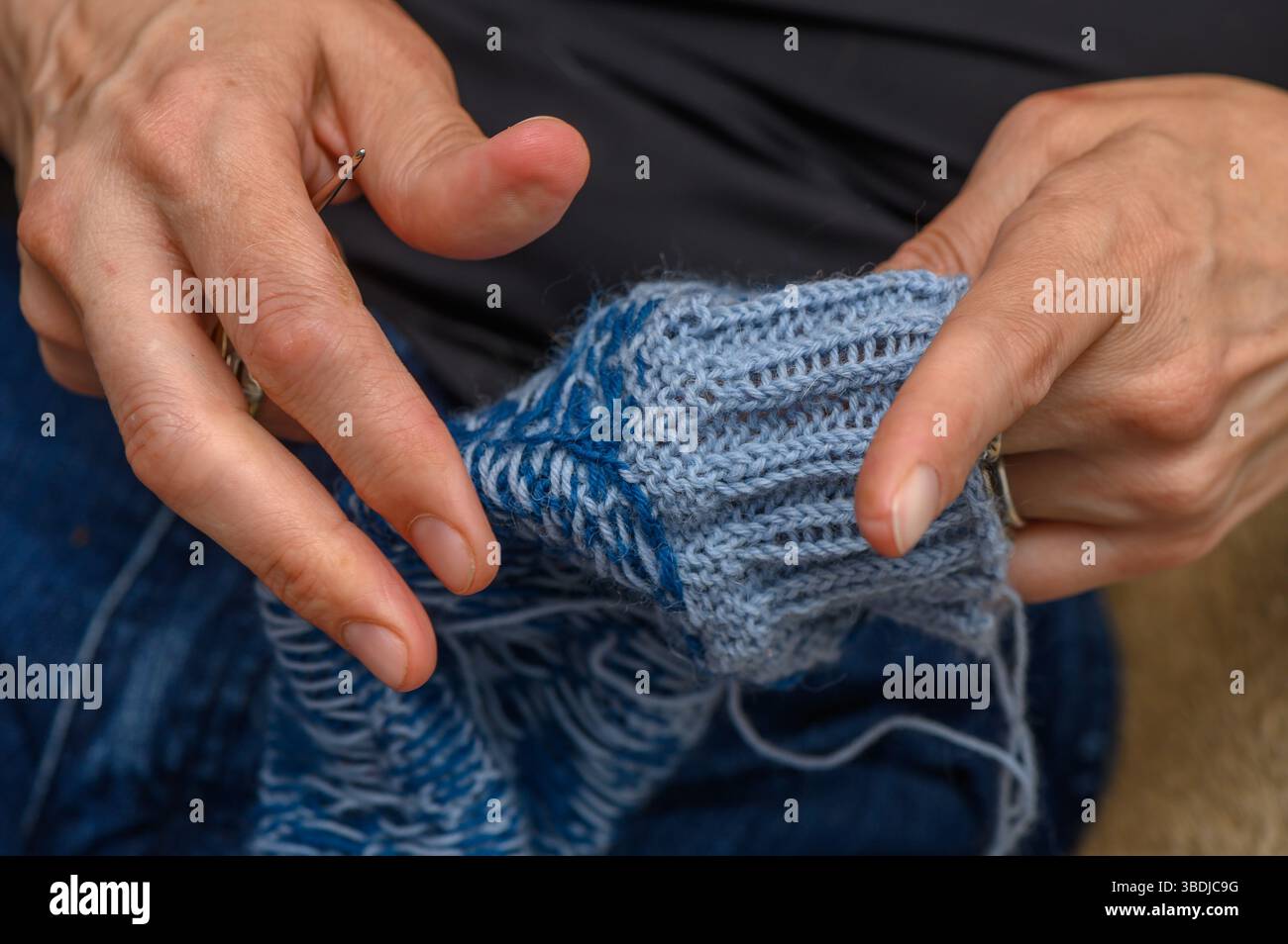 Nahaufnahme von Frauenhänden, die an einem gemütlichen Tag helle Wollsocken mit traditionellem Design stricken. Stockfoto