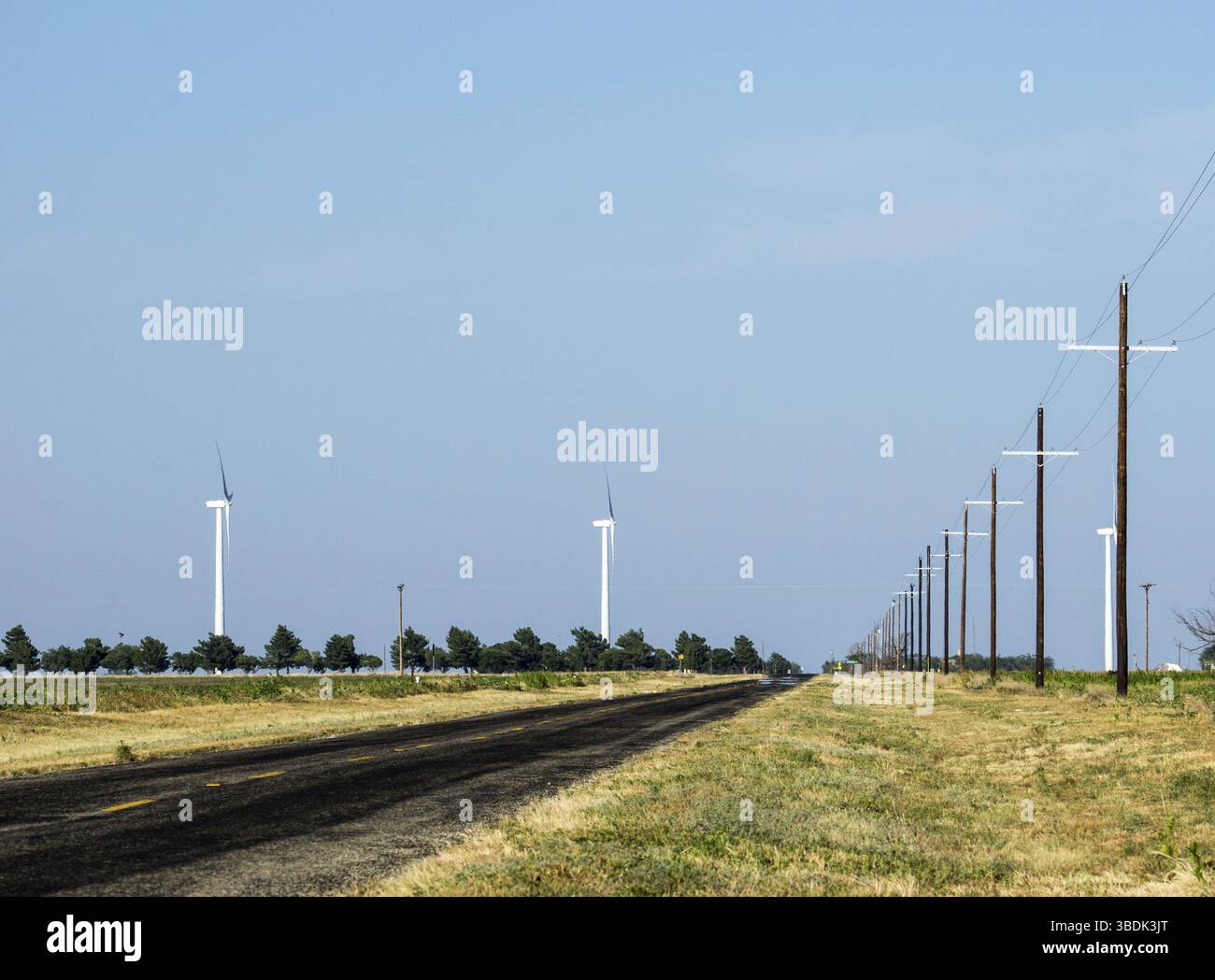 Landstraße in den leeren Texas prairie mit einer endlosen Weite des blauen Himmels und Stromleitungen direkt zu den Horizont und Windkraftanlagen, die in der d Stockfoto