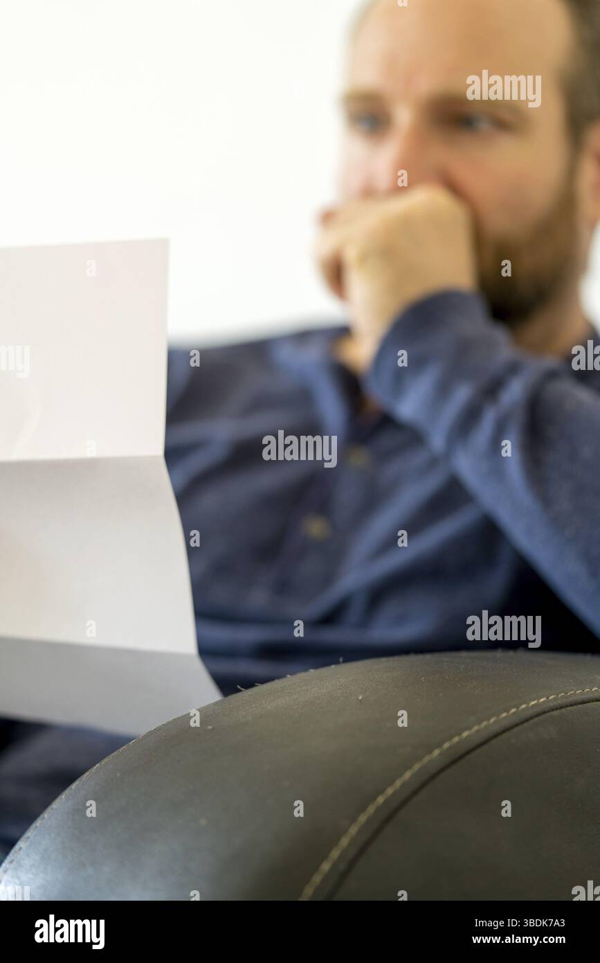 Mann in den Vierzigern sitzen auf einer Couch reachts emotional zu den schlechten Nachrichten, die er in einem Brief mit selektiven Fokus und kopieren Raum erhält Stockfoto
