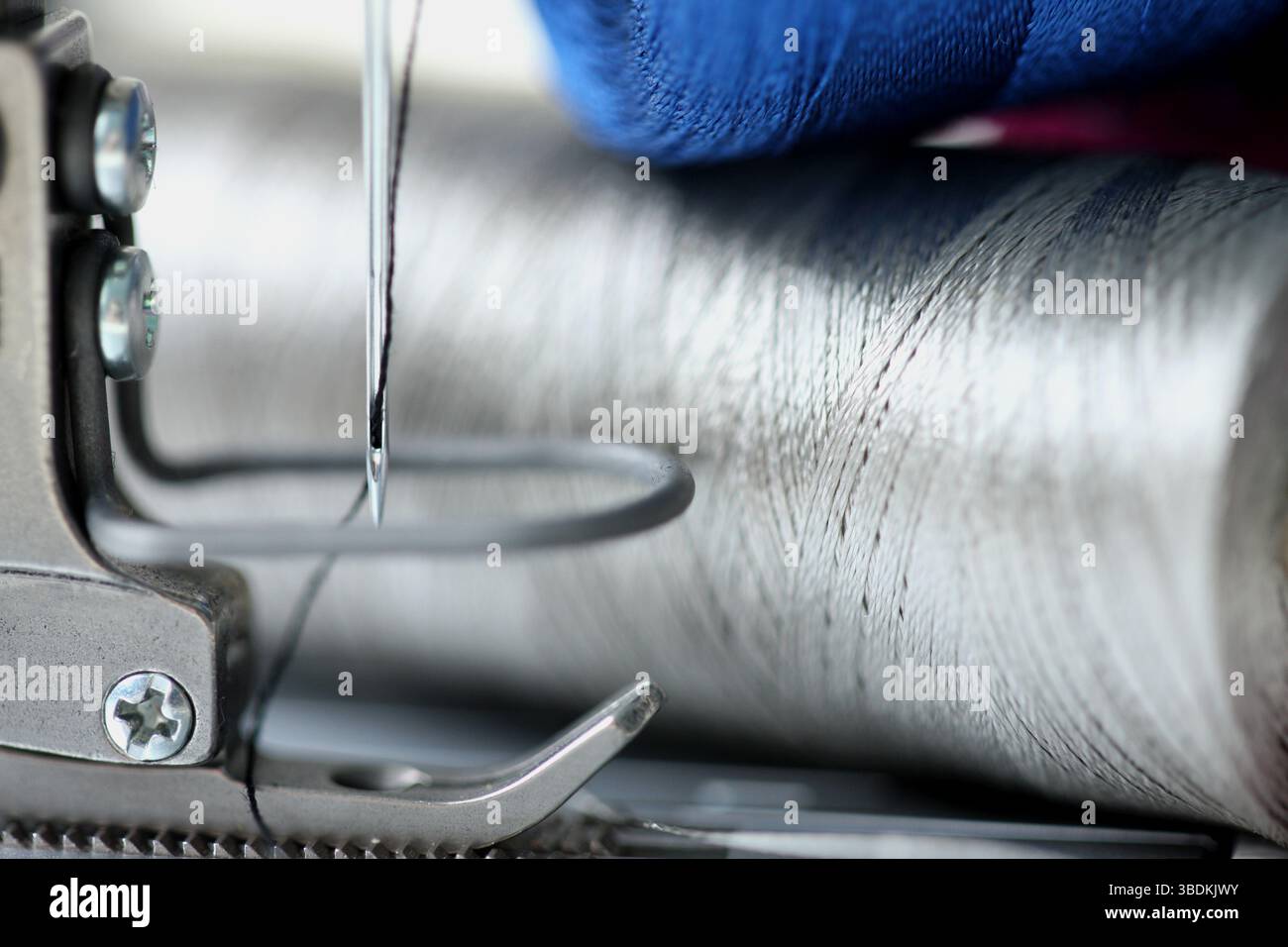 Nahaufnahme der Nadel und des Nähfußes für Reißverschlüsse mit natürlichem silbernem Metallgarn oder Garn der industriellen Nähmaschine. Kreatives Konzept. Stockfoto