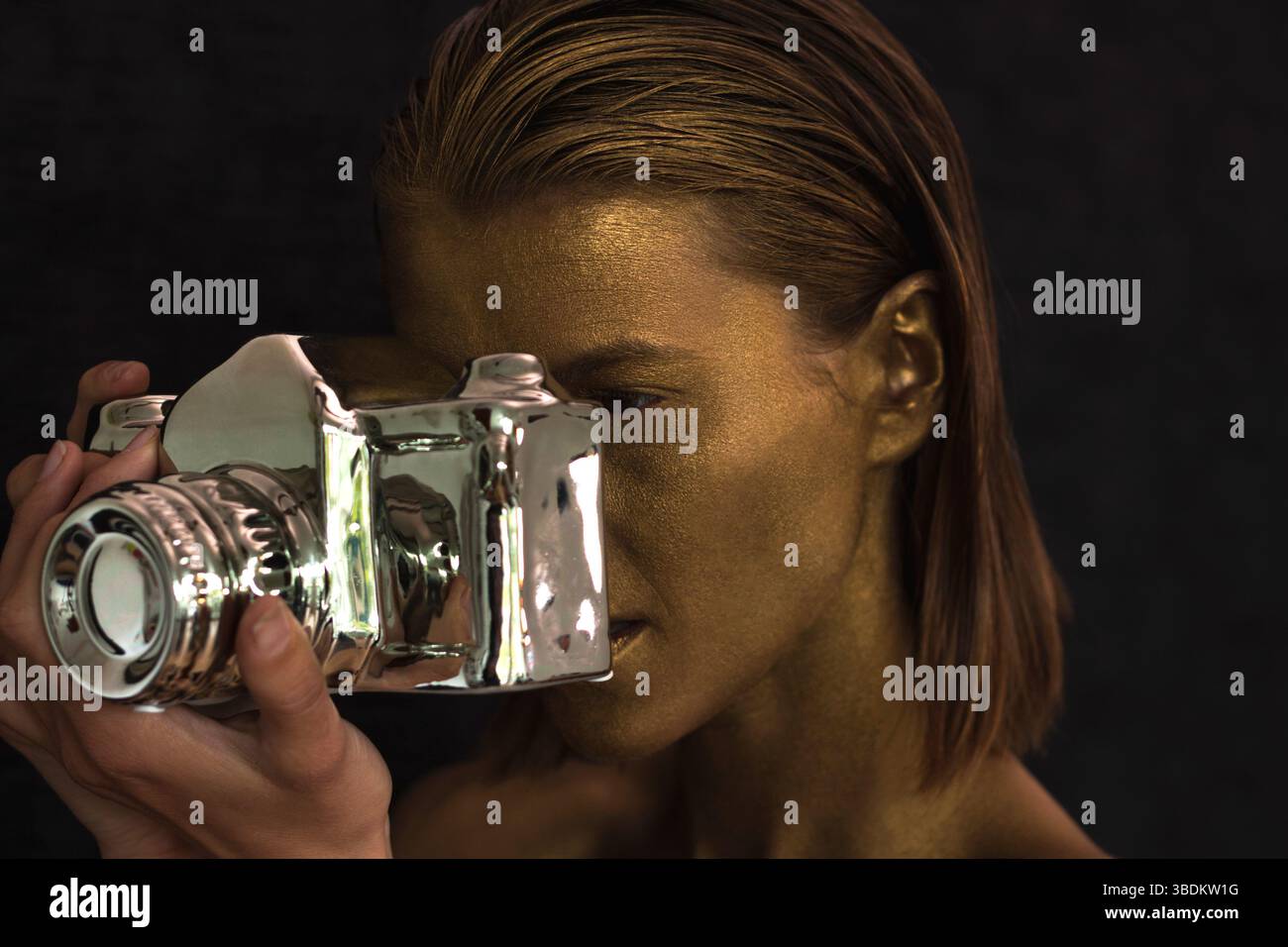 Porträt einer schönen jungen Frau mit Gesicht und Haut in Gold bemalt und mit silberner Keramikstatue als Dekoration, während Sie ein Foto machen. Stockfoto
