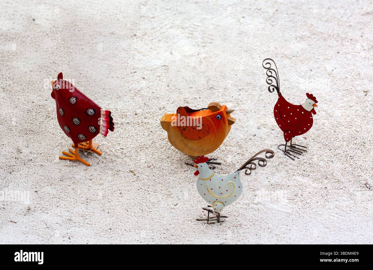 Auf sandigem Boden stehen Hühner und Gänsefiguren aus Metall, die rustikalen Charme wecken. Stockfoto