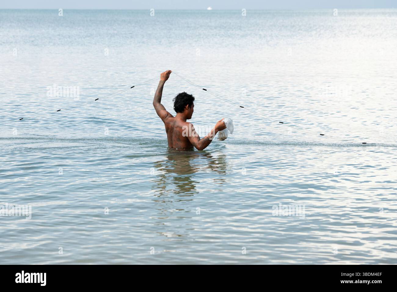 Pattaya, Thailand, 19. Oktober 2024: Ein Fischer steht in einer ruhigen See, hält eine Netzleine in der einen Hand und einen Plastikbeutel mit seinem Fang in der anderen. Stockfoto