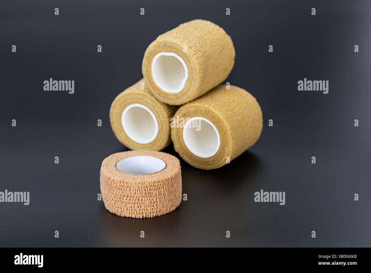 Vier elastische medizinische Verbandrollen sind auf dunkler Oberfläche gestapelt und zeigen ihre Textur und zylindrische Form. Diese Verbände werden häufig für verwendet Stockfoto