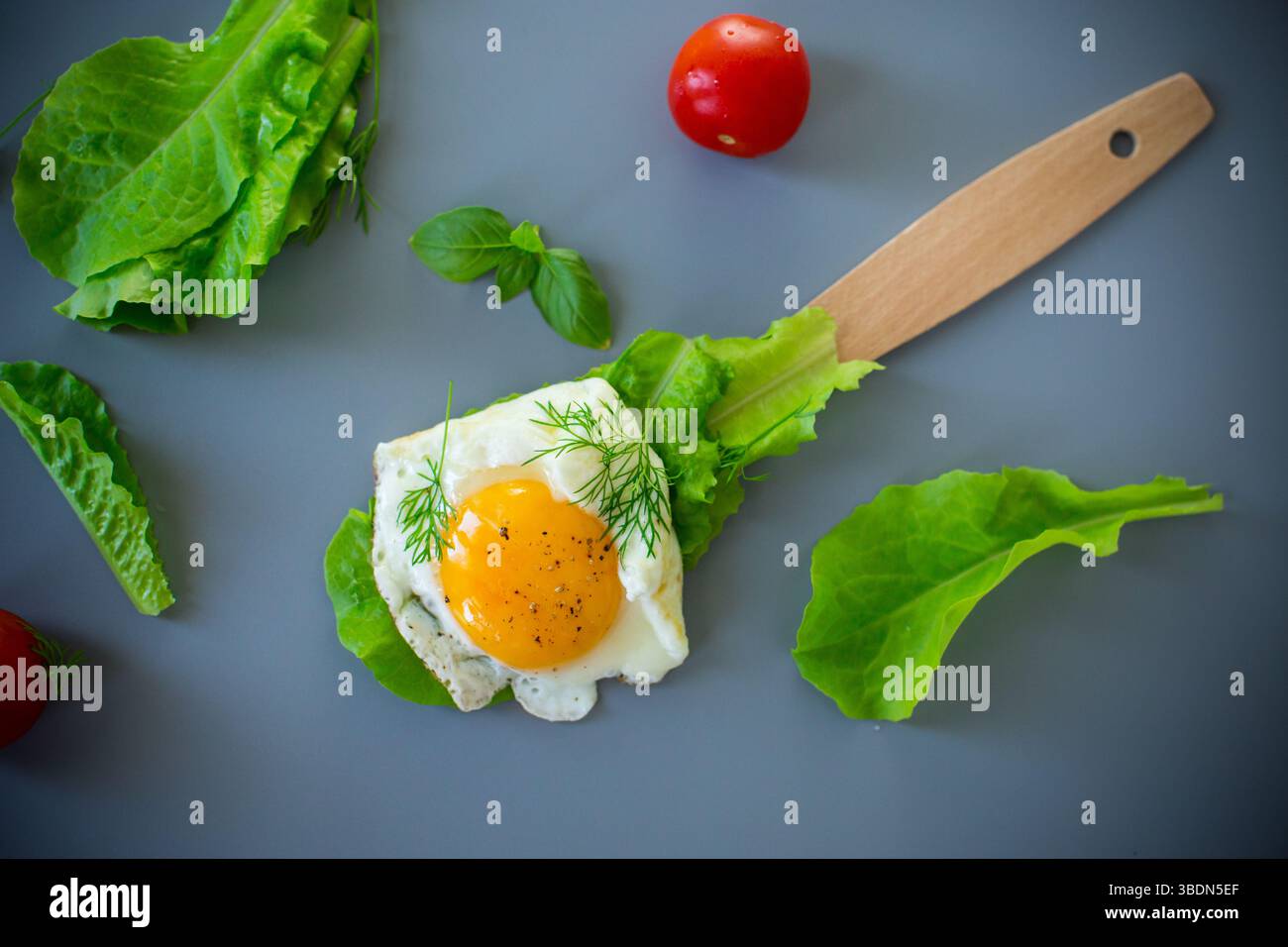 Nahaufnahme von leckerem Ei mit Salatblättern in der Küche, auf grauem Hintergrund. Stockfoto