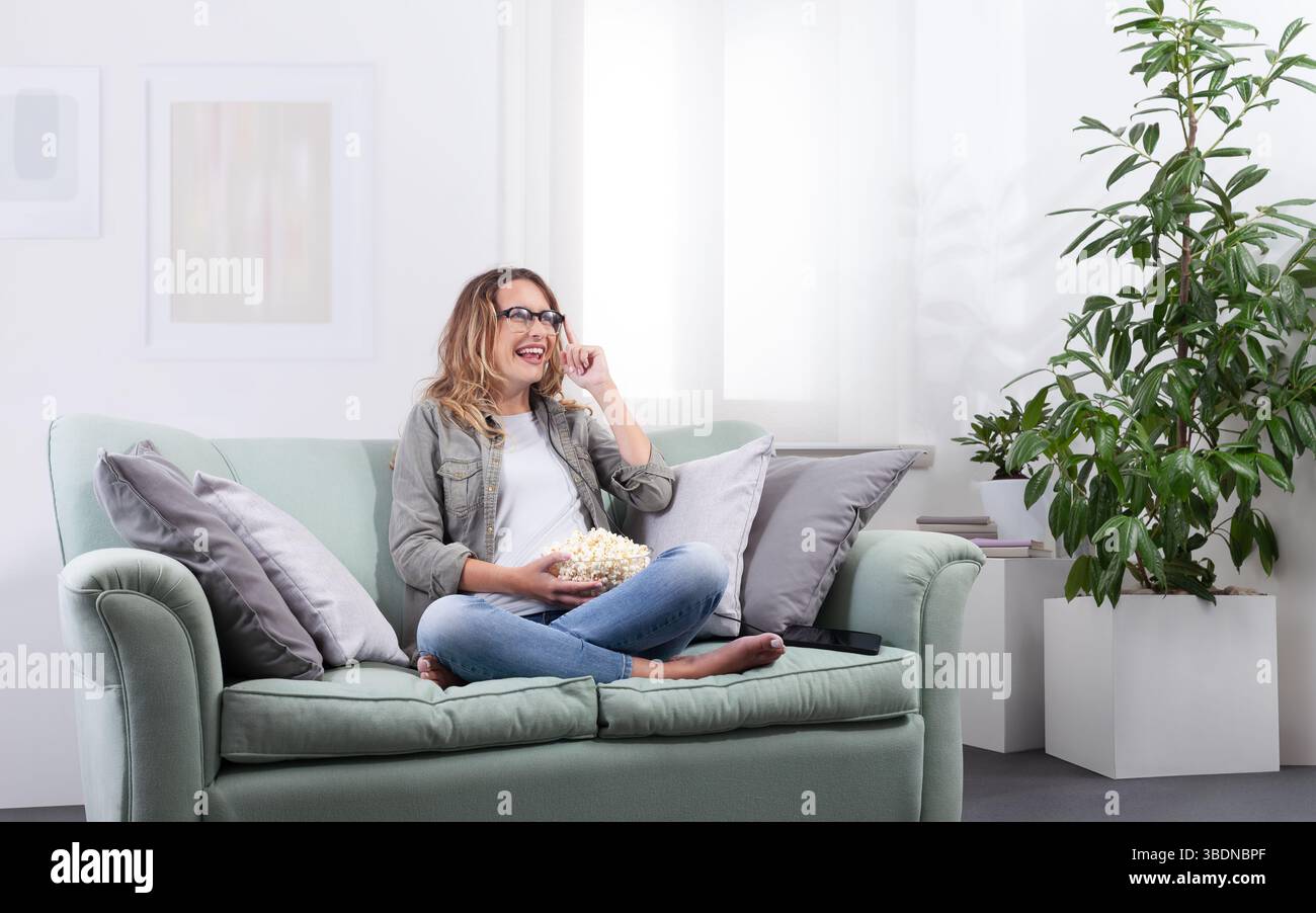 Eine Frau mit einer intelligenten Brille, die Popcorn hält und ihre Brille berührt, als ob sie mit einem virtuellen Display interagiert. Blick in den Weltraum mit digitalem und digitalem Stockfoto