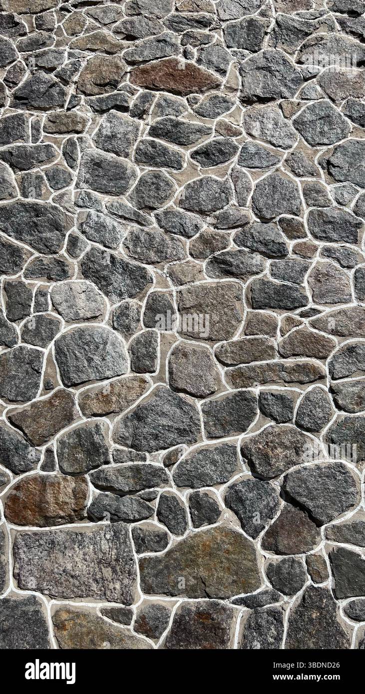 Graue Wand aus natürlichen Granitsteinen. Ein einzigartiger moderner Zaun. - Smartphone-aufgenommenes Stockfoto