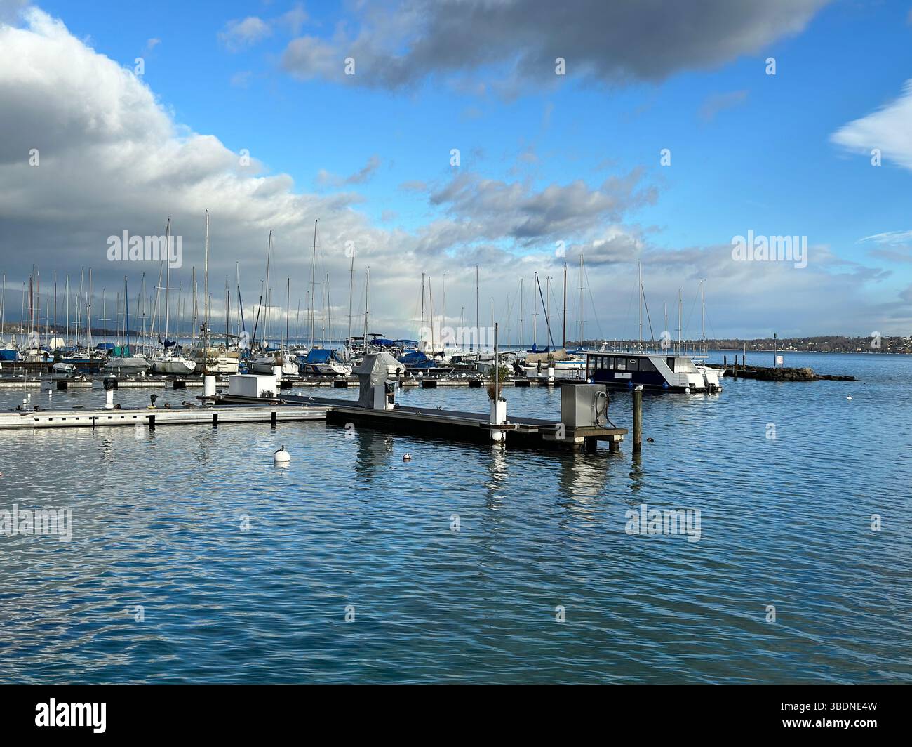 Eine friedliche Hafenszene Genf mit Booten unter einem hellblauen und bewölkten Himmel, perfekt für einen sonnigen Tag. Stockfoto