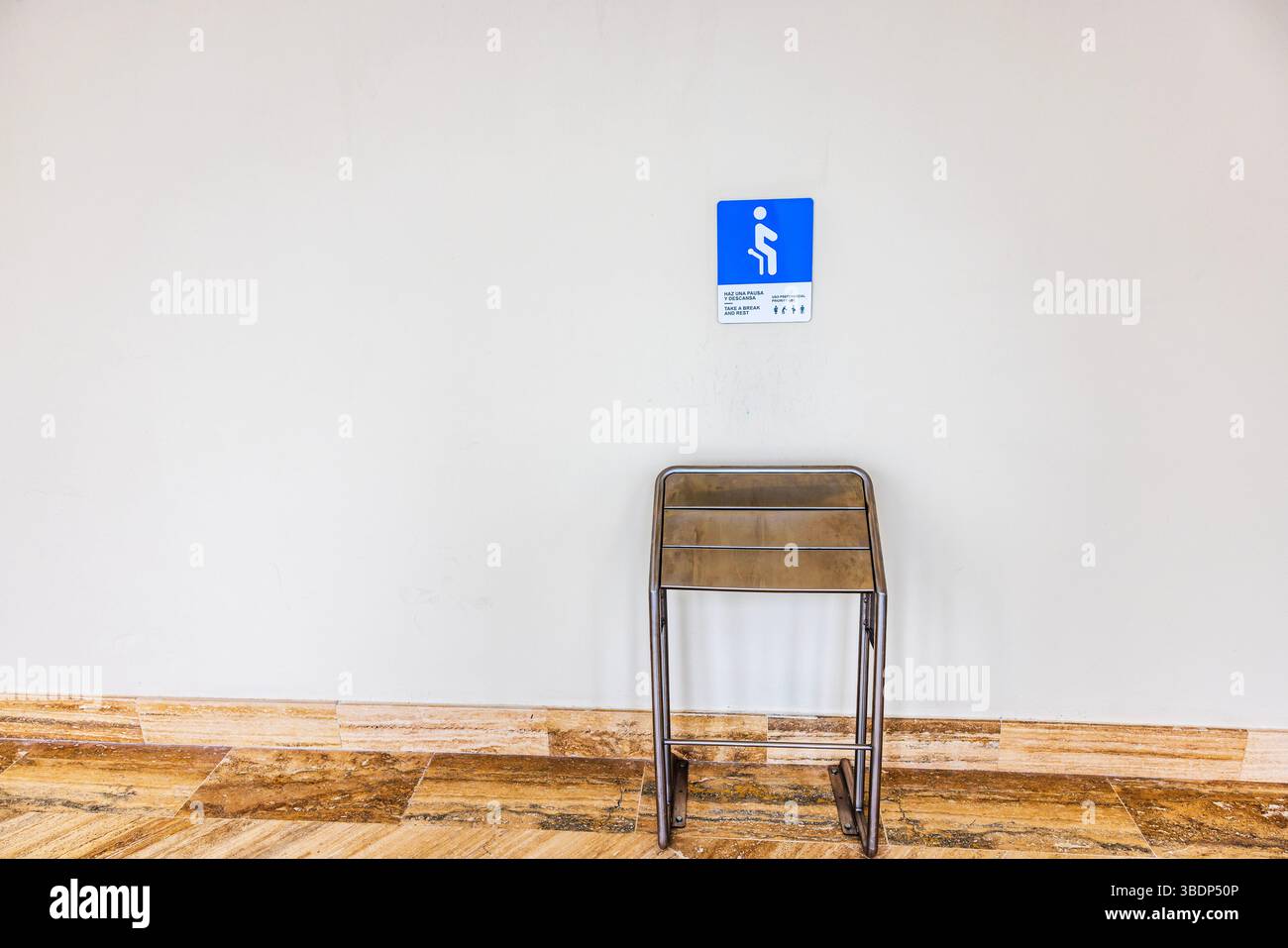 Metallstuhl, der an der Flughafenwand unter dem blauen Prioritätenschild auf Steinfliesen gefaltet ist. Punta Cana. Dominikanische Republik. Stockfoto