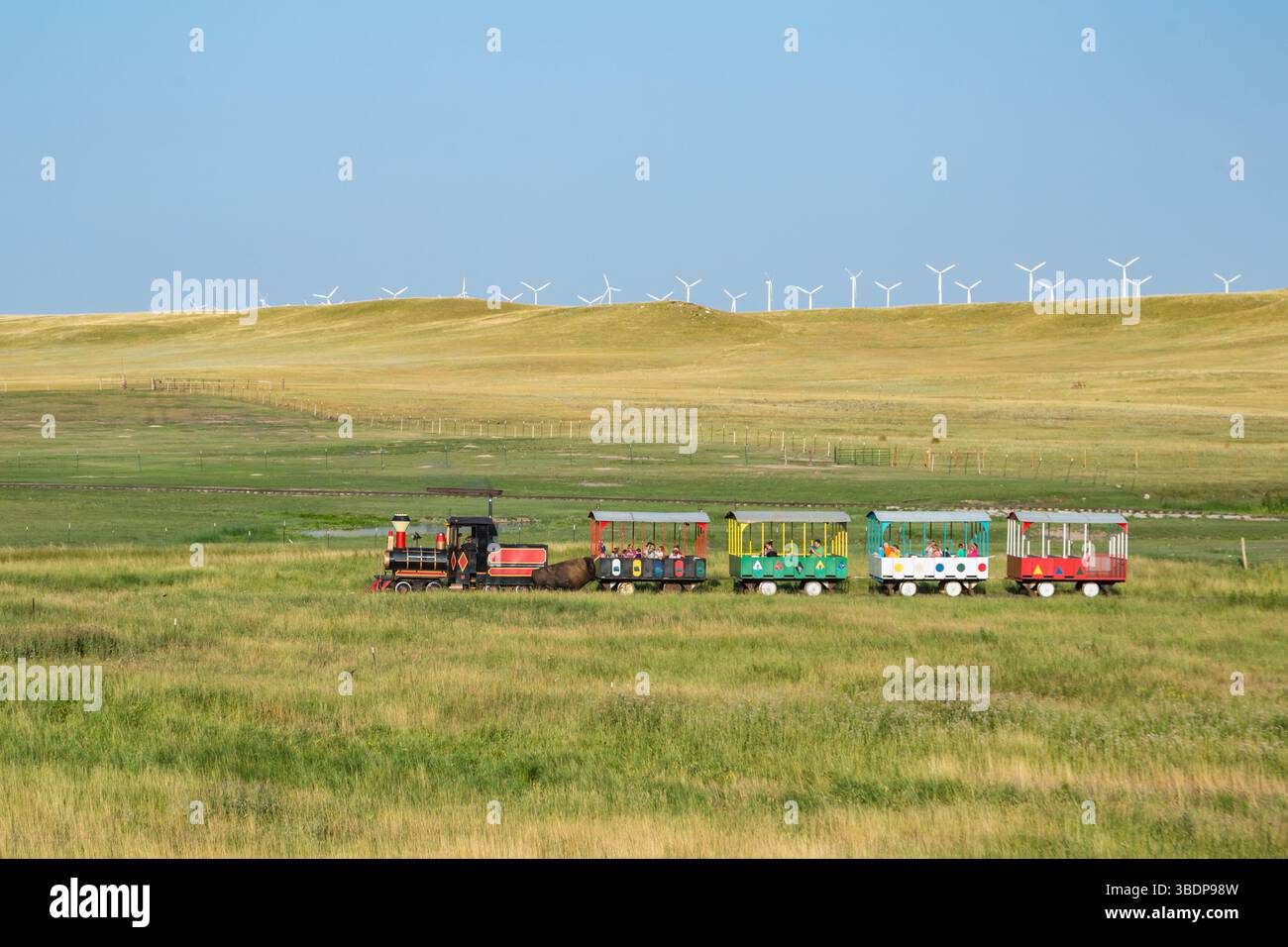 Windmühlen mit grüner Energie hinter einer Bison-Zug-Tour, die Besucher auf der Terry Bison Ranch in der Nähe von Cheyenne, Wyoming, durch die Weide führt, auf der Bisons herumlaufen Stockfoto