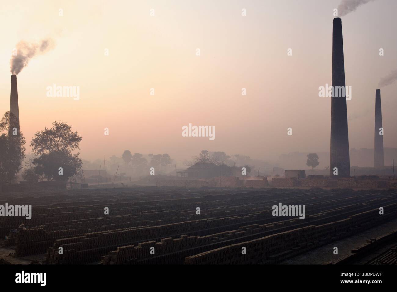 Nebel und Rauch der Dämmerung verschließen Ziegelöfen und Trockenfelder in einer Fabrik in Gazipur, Bangladesch, und enthüllen die atmosphärische Belastung von Ziegelsteinen im industriellen Maßstab. Stockfoto