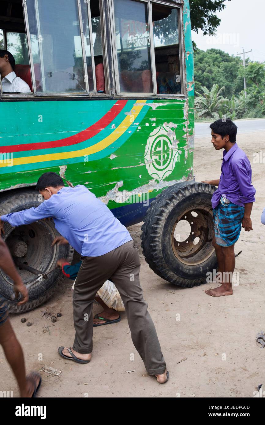 Männer reparieren einen Reifenpanne in einem abgenutzten Überlandbus in der Nähe von Tangail, Bangladesch, und enthüllen die informellen Arbeitskräfte, die den Straßenverkehr unterstützen. Stockfoto