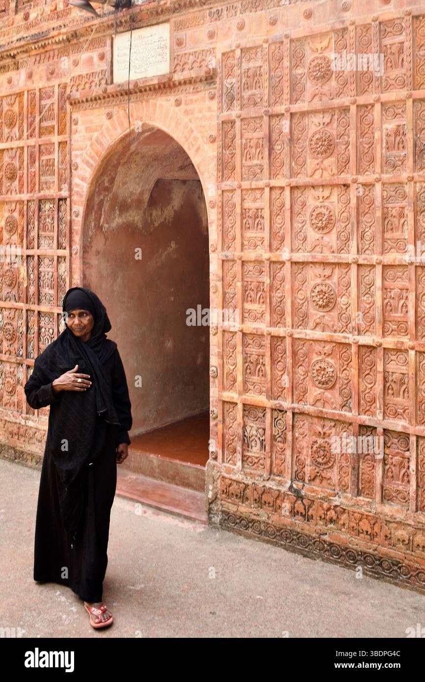 Eine Frau in schwarzer Kleidung passiert den mit Terrakotta geschmückten Eingang der Atiya-Moschee aus dem 17. Jahrhundert in Tangail, Bangladesch. Stockfoto