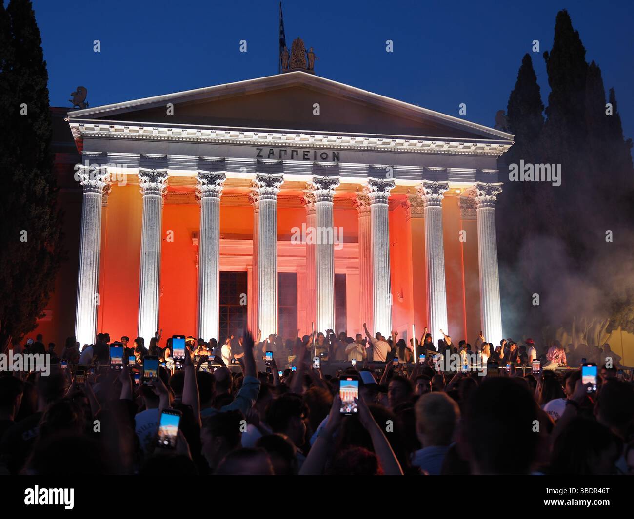 Athen, Griechenland - 3. Mai 2025: Zappeion beleuchtet bei Nacht mit orangefarbenem Licht, umgeben von einer großen Menschenmenge während des Athens City Festivals 2025 Stockfoto Athen, Griechenland - 3. Mai 2025: Zappeion beleuchtet bei Nacht mit orangefarbenem Licht, umgeben von einer großen Menschenmenge während des Athens City Festivals 2025 Stockfoto