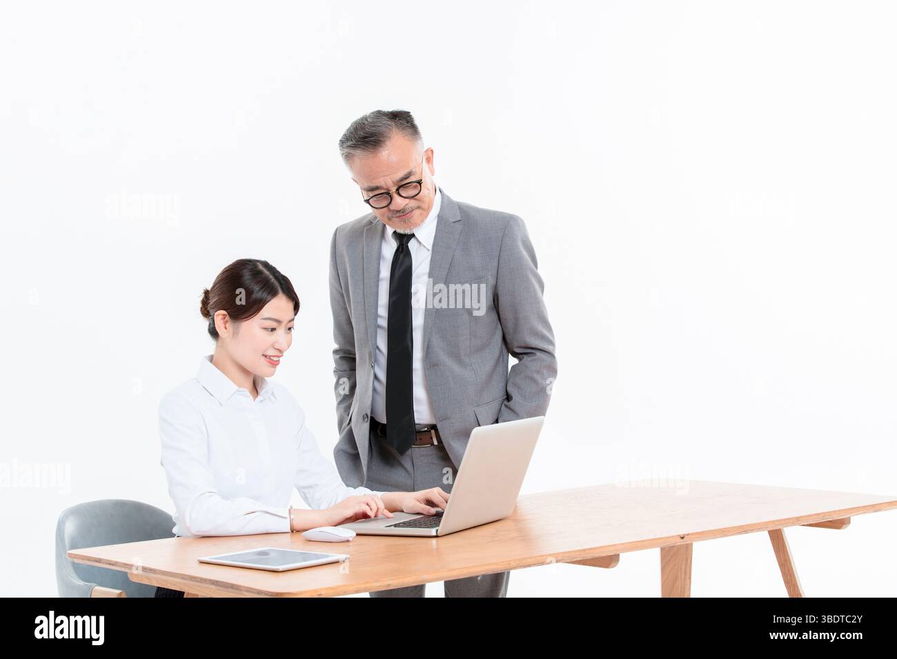 Ein geschäftlicher älterer Mann und eine junge Frau stehen (sitzend) am Schreibtisch Stockfoto