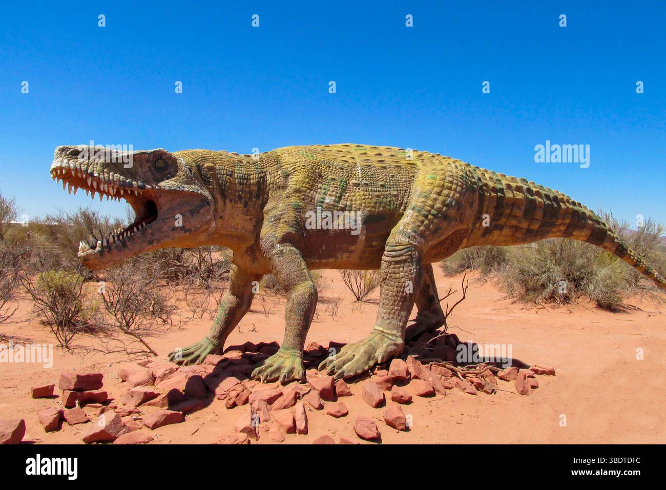 Dinosaurier im Wüstenland. Die Statue, ein Modell-Dinosaurier, der auf einem roten trockenen Sand zwischen den Felsen steht. Künstlicher Dinosaurier. Jurassic Park. Modelle Dino Stockfoto