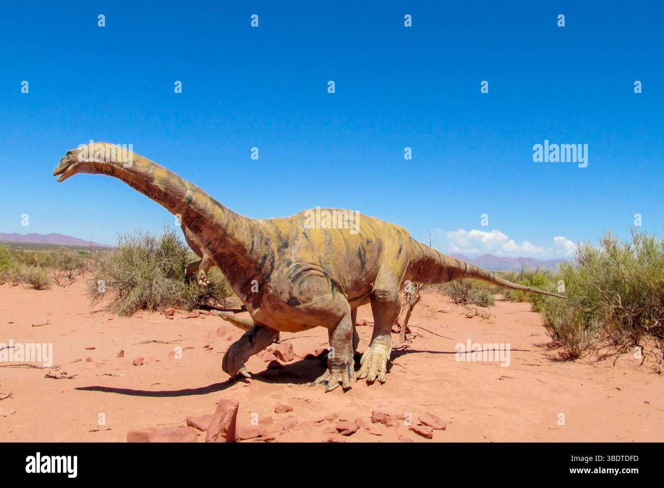 Dinosaurier im Wüstenland. Die Statue, ein Modell-Dinosaurier, der auf einem roten trockenen Sand zwischen den Felsen steht. Künstlicher Dinosaurier. Jurassic Park. Modelle Dino Stockfoto