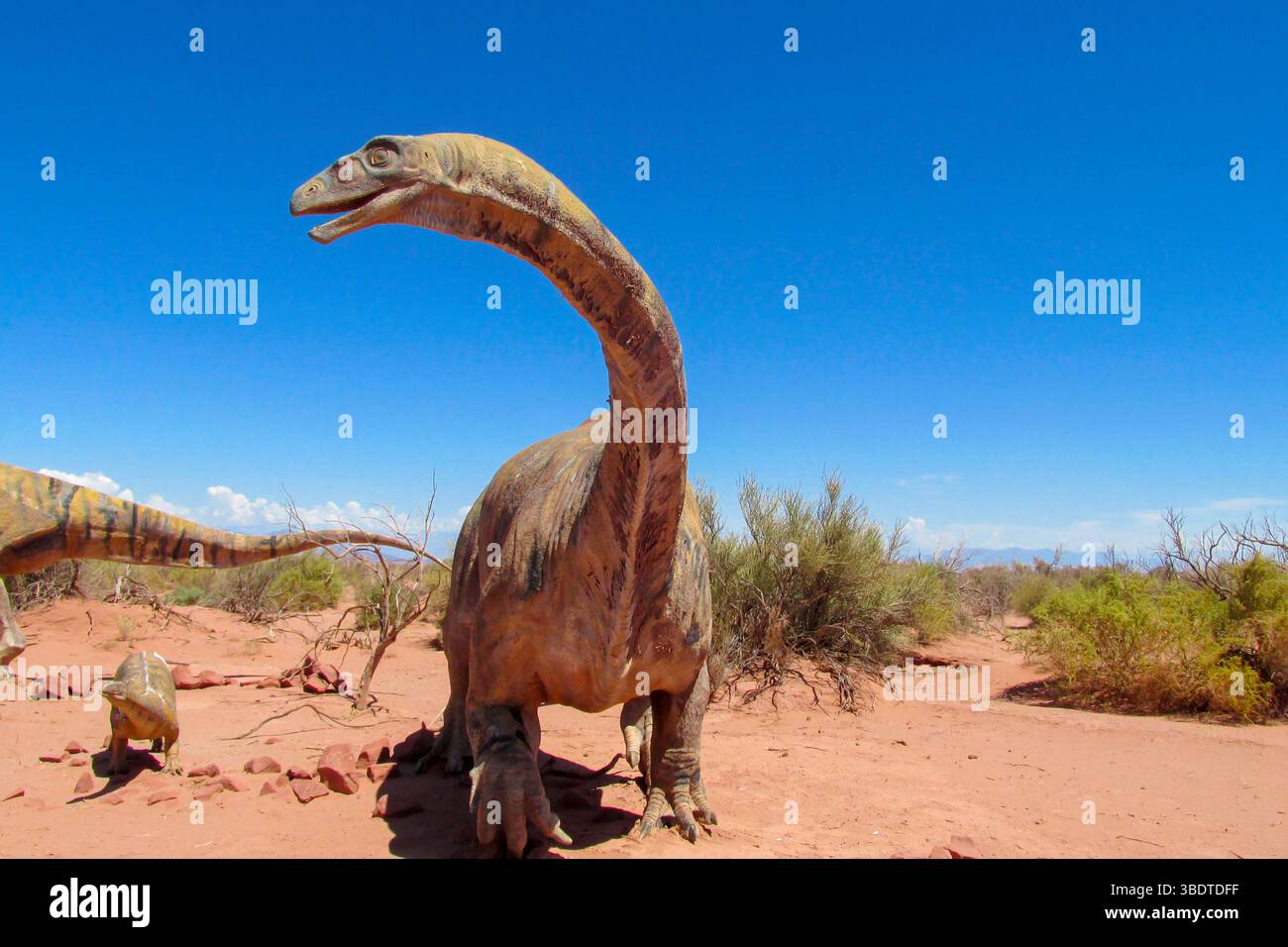 Dinosaurier im Wüstenland. Die Statue, ein Modell-Dinosaurier, der auf einem roten trockenen Sand zwischen den Felsen steht. Künstlicher Dinosaurier. Jurassic Park. Modelle Dino Stockfoto