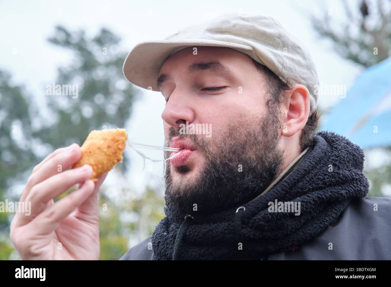Junger Mann genießt im Freien frisch zubereitete Empanada aus argentinischem Schinken und Käse. Stockfoto