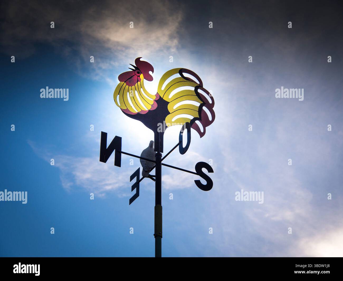 Ein Wetterhahn mit einem hellen Hahnendesign sitzt hoch auf einer Stange, die sich vor einem dramatischen Himmel abhebt. Frankreich Stockfoto