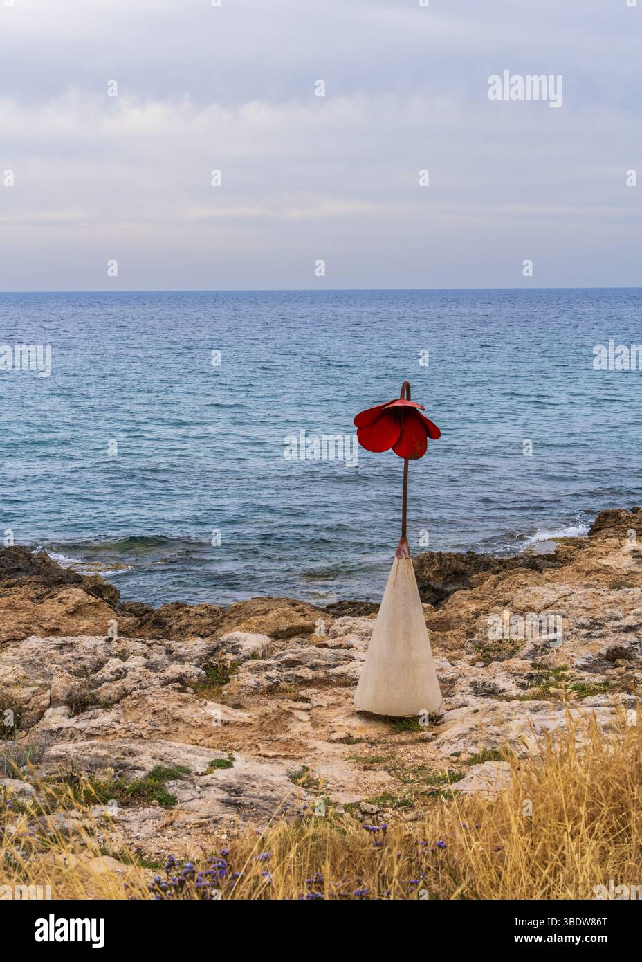 Eine Steinblume in Form eines roten Mohns am felsigen Ufer von Paphos, Zypern. Straßenlaterne am Meer. Stockfoto