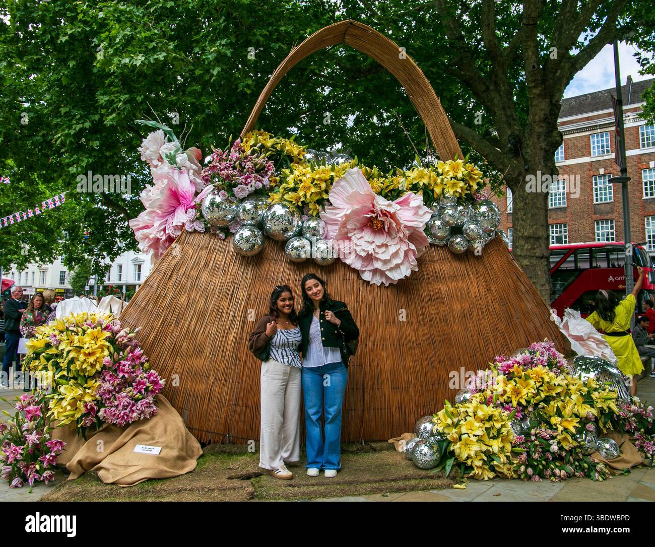 Zwei Frauen posieren glücklich vor einem riesigen Korb mit großen Blumen und silbernen Dekorationen. Chelsea in Blüte 2025 Duke of York Square Stockfoto